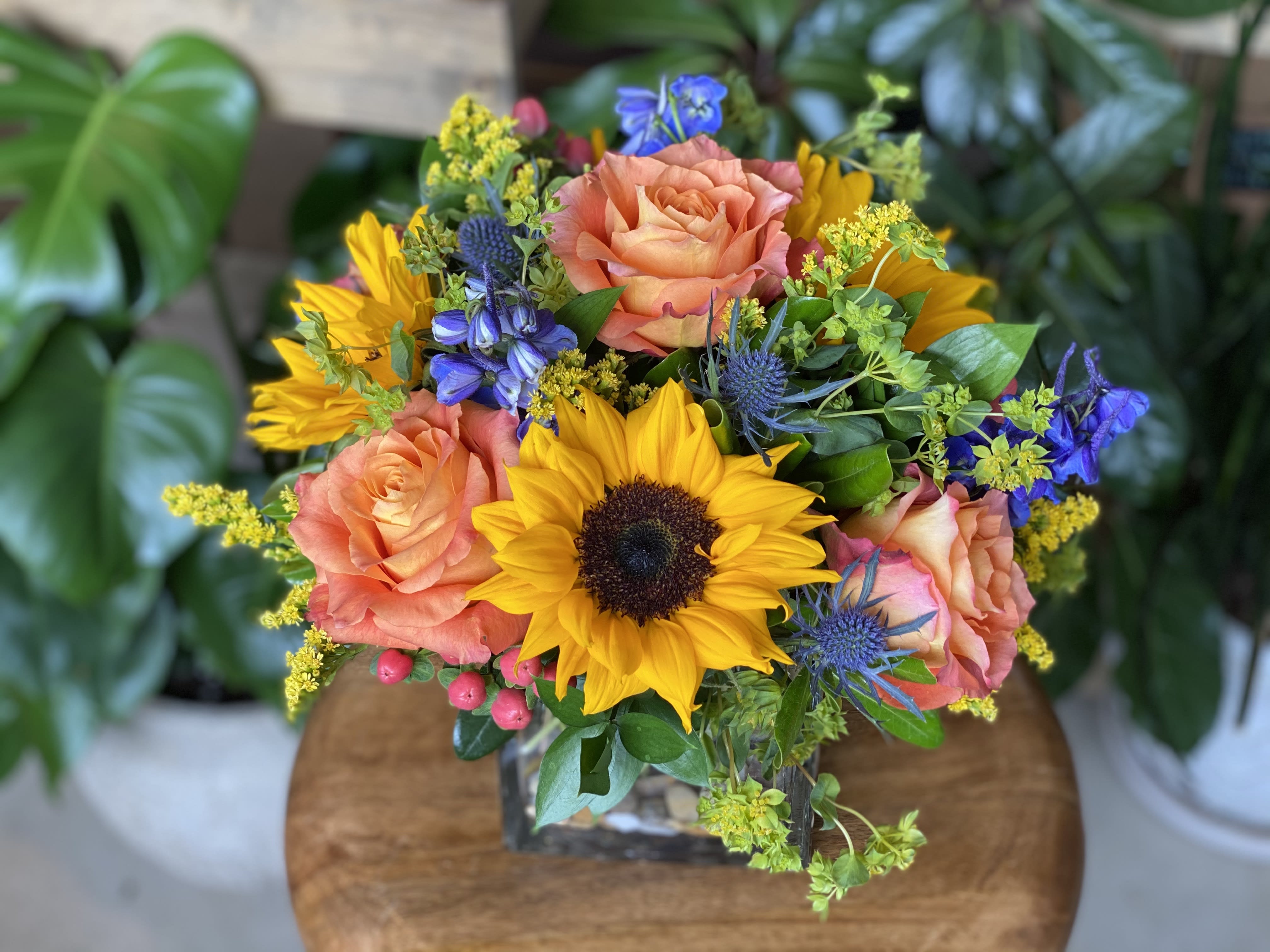 The Chelsea by Simply Fresh Flowers - The Chelsea is a cheery design of sunflowers, roses, delphinium, thistle, hypericum &amp; accent blooms arranged in a cubed vessel. A simply sun-filled arrangement sure to make anyone smile!