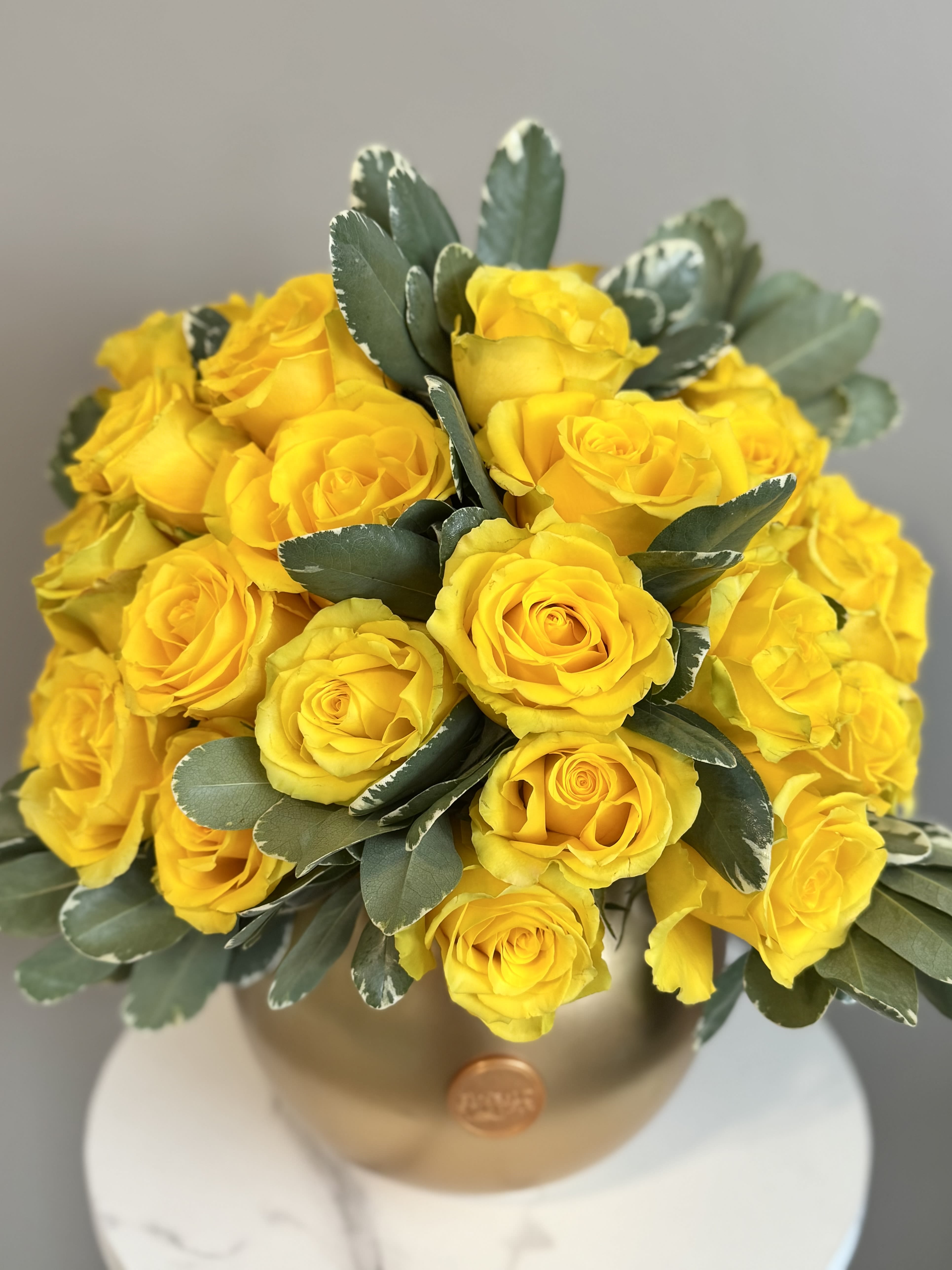Golden Glow - Brighten any room or occasion with the radiant beauty of Golden Glow. Featuring approximately 3 Dozen vibrant yellow roses, this arrangement is a perfect symbol of joy, optimism, and elegance. Designed in a sleek gold-tone vase, it exudes timeless sophistication with a modern twist.  Whether you’re celebrating a special moment or simply adding a touch of sunshine to someone’s day, Golden Glow is sure to leave a lasting impression. A celebration of beauty and positivity in every petal.
