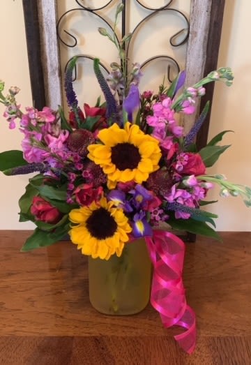 Embrace This Day - A mixed fresh cut consisting of Sunflowers, Purple Iris, Pink Stock, Purple Larkspur, Scabiosa, Pink Wax Flower, Purple Veronica, and Fuchsia Alstromeria.  If you like the look and style of this arrangement but have a smaller budget, head on over to our Designer's Choice Option and choose the budget that suits your needs best.  We will be happy to make a smaller version for you of arrangements that we currently have available in stock.  Let us know which one you are interested in when placing your order.