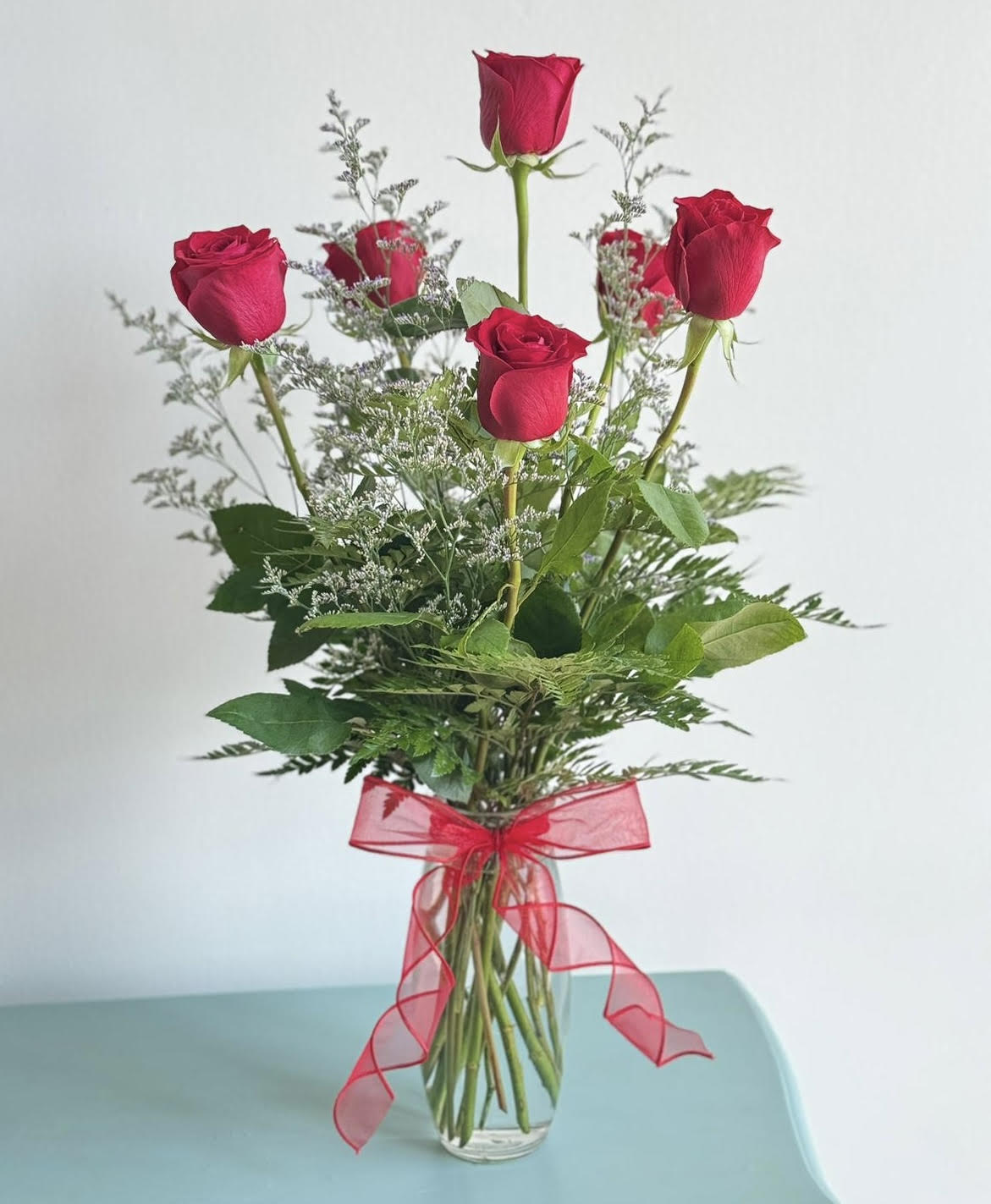 Half dozen of Roses - Six exquisite red roses arranged with tropical foliage in a clear bud vase.