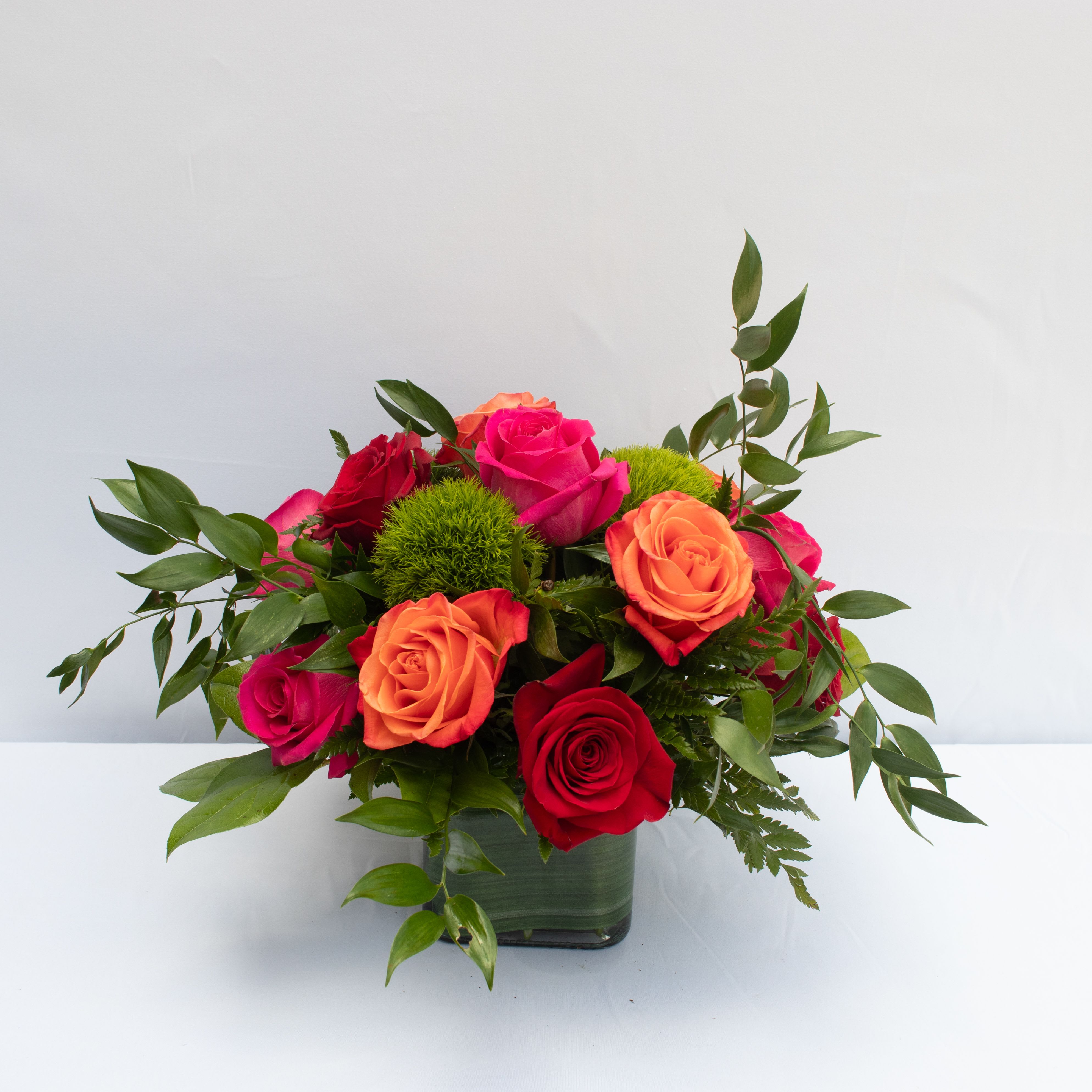 Lush Life Rose Bouquet - We only use the best Ecuadorian Roses on the market.  Rich in color and unmatched beauty this blushing rose bouquet flaunts a modern styling to send your warmest heartfelt wishes to your recipient in a way they will never forget. Hot pink, orange, and red roses capture the eye and the imagination accented with green trachelium bupleurum and ivy vines for a fresh look. Presented in a clear glass cubed vase lined with ti green leaf material to add to the overall display this fresh flower arrangement is ready to celebrate a birthday or anniversary or send your thank you or get well wishes in style.