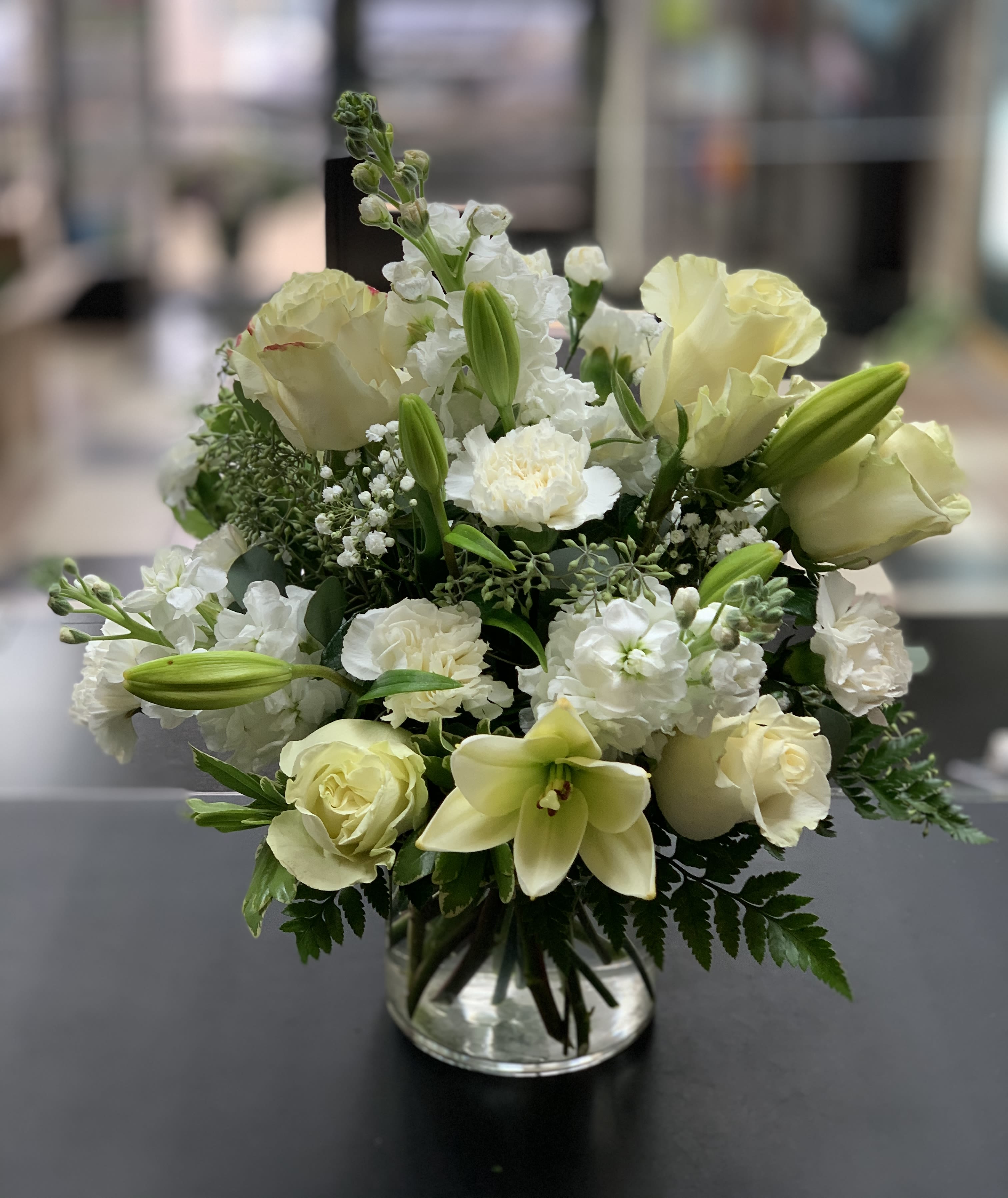 Peaceful clouds - Stunning white roses, lilies, mums, carnations, daisy poms and more, expertly arranged in a clear glass cylinder lined with a Ti leaf ribbon. 12&quot;H x 11&quot;W