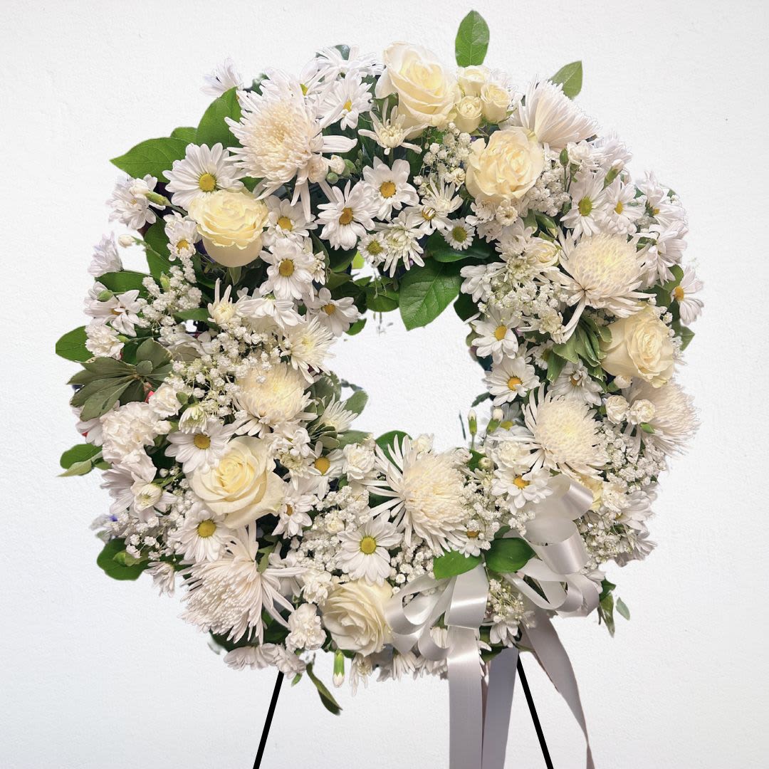 White Serenity Wreath - Express your heartfelt sympathy with our White Serenity Wreath. This elegant wreath features a harmonious arrangement of pristine white roses, chrysanthemums, and delicate sprigs of baby's breath, symbolizing peace and purity. This gentle and comforting tribute offers solace and serves as a beautiful memorial to honor the memory of a loved one.