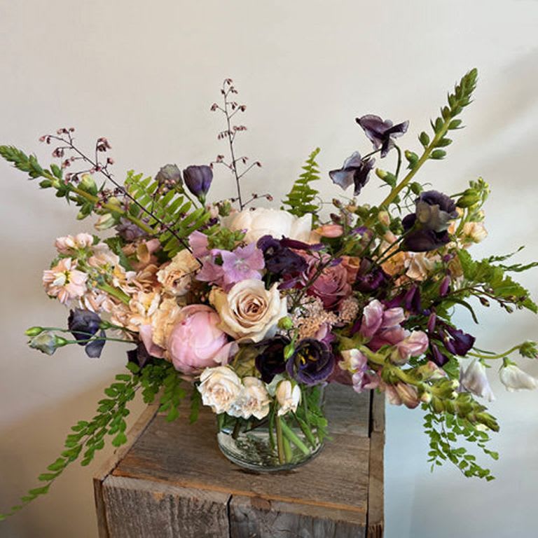 Lavender Blue Lavender Blue - A soft yet striking combination of lavender, blush and plum in a mix of seasonal blooms. PLEASE NOTE: Flower colors and varieties will vary due to availability but the over all aesthetic of the arrangement will stay the same. Our designers always select the freshest blooms for your arrangement. Standard - 5" cylinder vase with a lush mix of seasonal blooms. Measures approximately 10" tall and 10" wide. Deluxe - 6" cylinder vase with a lush mix of seasonal blooms. Measures approximately 12" tall and 12" wide Premium - 8" cylinder vase or other similar sized vase with a lush mix of seasonal blooms. Measures approximately 15"+ tall and wide. Deluxe version is pictured