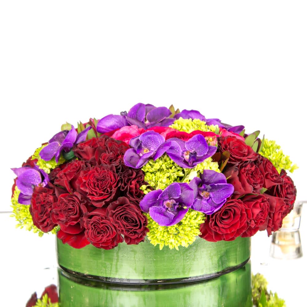 Rich Rendezvous - Feminine colors, flowers and textures are all wrapped up in this rich floral arrangement. Red Roses, Violet Vanda Orchids and Green Hydrangeas are beautifully arranged in a round leaf lined glass vase. Understated and striking at the same time, it is a gorgeous gift that is sure to make a statement! Approx: 12&quot; W x 4&quot; H 