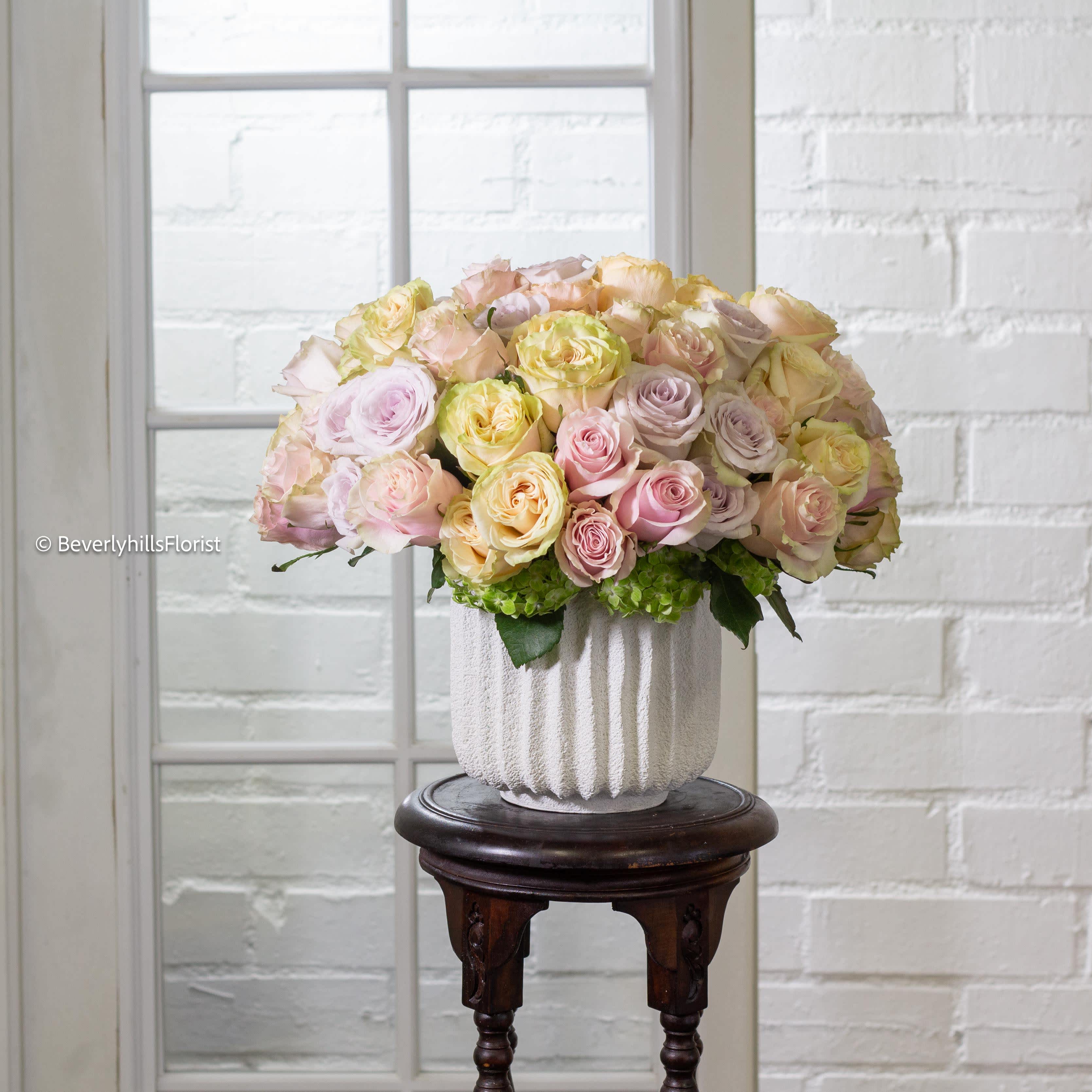 Ethereal Pastels - In a pristine white vase, a delicate array of pastel roses blooms with ethereal beauty. Each petal whispers softly in shades of pale pink, soft lavender, and gentle peach, evoking a sense of tranquility and grace. This enchanting arrangement exudes a serene elegance, bringing a touch of serenity and sweetness to any setting.
