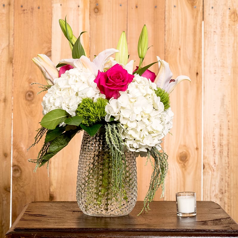 Astin Gardens Bouquet - This luxurious collection of flowers looks as though they were just plucked from the garden!! A beautiful presentation of  white hydrangeas, hot pink roses, fragrant oriental lilies, green dianthus and faux moss in a clear glass vase. Another original design that is definitely elegant and tasteful!!