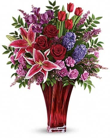 One Of A Kind Love Bouquet by Teleflora - For a love that's truly one of a kind. Celebrate your unique bond this Valentine's Day with this magnificent bouquet of roses, lilies, alstroemeria and more, artfully arranged in an elegant red blown-glass vase. Dazzling with graceful details, it's a true dÃ©cor piece they'll enjoy forever as a resplendent reminder of your love. Red roses, red tulips, pink stargazer lilies, purple alstroemeria, pink miniature carnations, and lavender hyacinth are arranged with pink heather, huckleberry and lemon leaf. Delivered in a gorgeous Love's Passion vase.