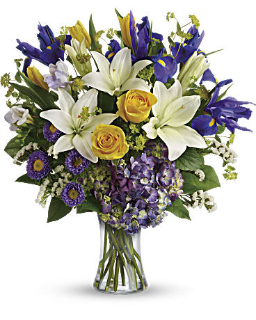 Teleflora's Floral Spring Iris Bouquet - This luxurious mix of hydrangea, roses, tulips, lilies and irises brings the glory of a fresh spring sky to any occasion! What a majestic mix of blues, yellows and whites, gracefully gathered in a classic glass vase. Purple hydrangea, yellow roses, yellow tulips, white asiatic lilies, blue iris, lavender freesia, and lavender matsumoto asters are arranged with white sinuata statice, bupleurum, and lemon leaf. Delivered in a Clear Glass Gathering Vase.
