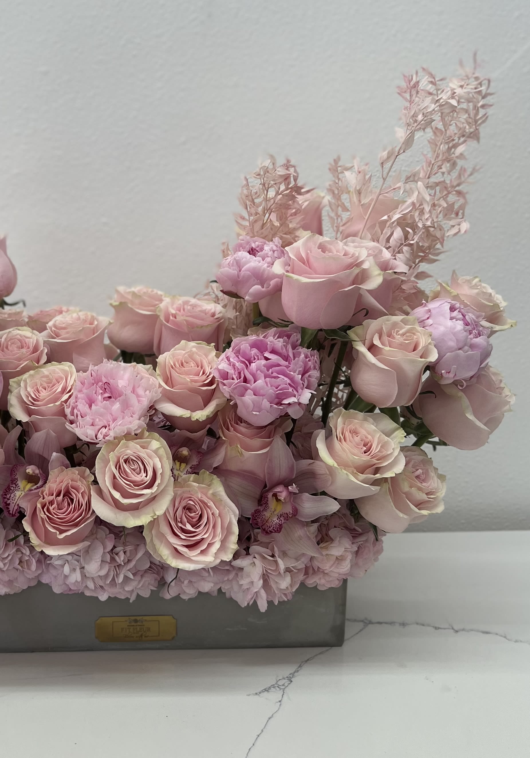 Lush Pink  -   Surprise your loved one with our breathtaking grand arrangement featuring a vibrant mix of luxurious roses and delicate peonies. This eye-catching display is designed to make a bold statement, perfect for anniversaries, birthdays, or just because you want to show how much you care.  Each arrangement showcases the lush beauty of velvety roses, complemented by the soft, ruffled petals of fresh peonies, creating a stunning contrast that captivates the senses. The rich colors and fragrant blooms evoke feelings of romance and admiration, making this a truly unforgettable gift.  Skillfully arranged to highlight the natural beauty of each flower, this grand bouquet is perfect for placing in a prominent spot where it can be admired and cherished. Whether it’s for a special occasion or a spontaneous gesture of love, this arrangement is sure to amaze and delight your loved one, leaving them with a lasting impression of your thoughtfulness and affection. Celebrate love in all its forms with this exquisite floral masterpiece!