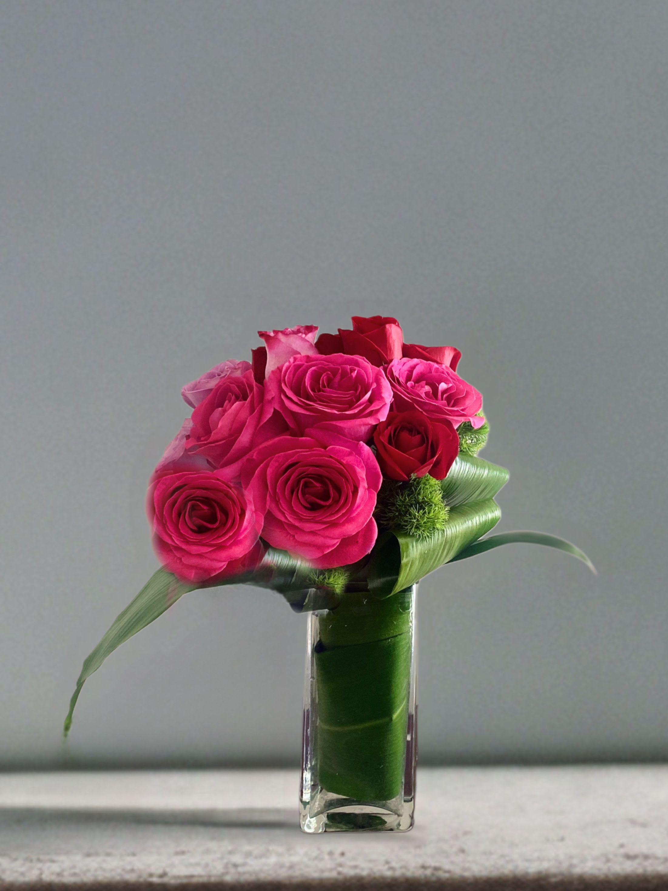 Wrapped in Love Bouquet  - Stylized red and pink roses with rich leaves and foliage in a tall glass rectangle. 