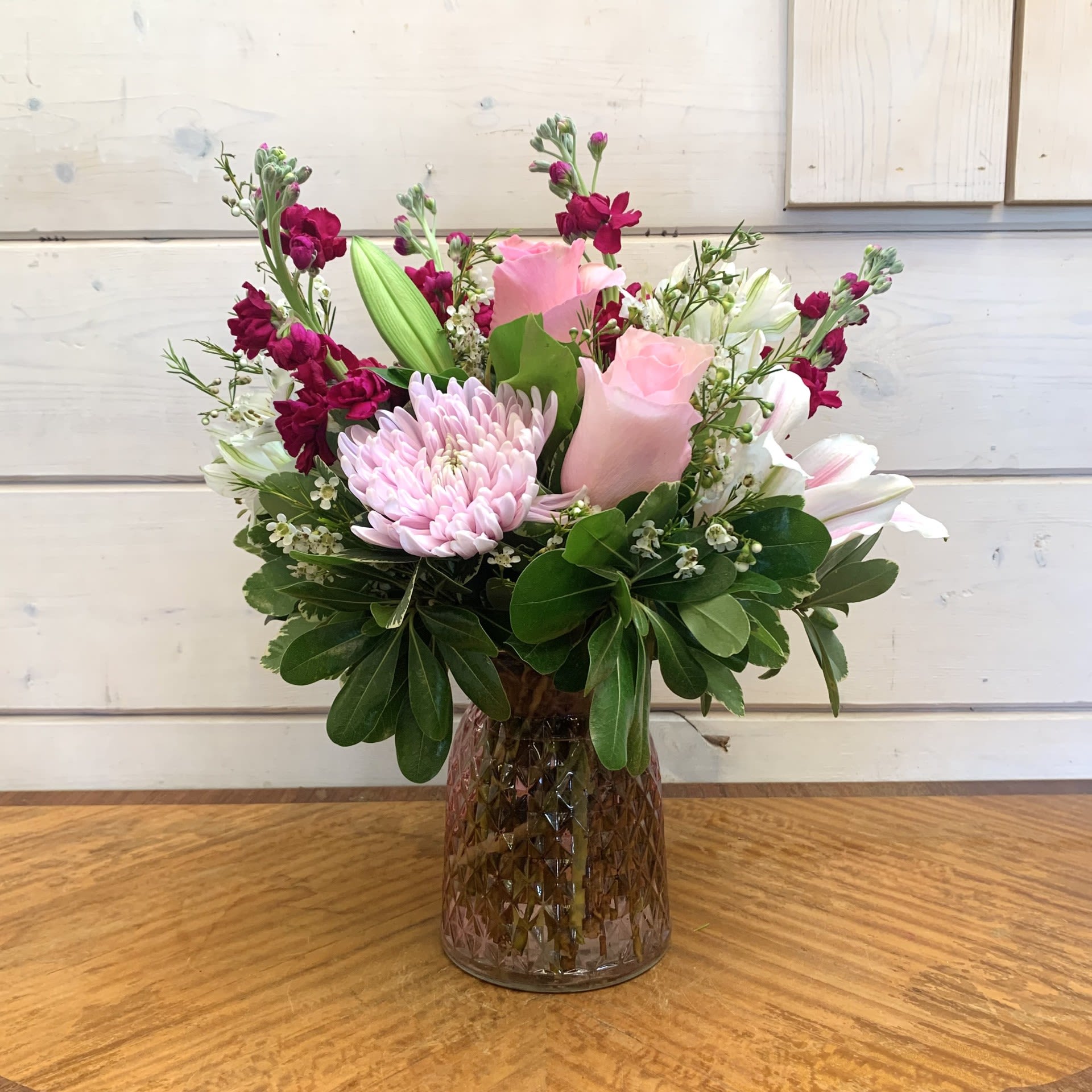 Blushing Bashful Bouquet - Pale pink roses arranged with fragrant magenta stock, stargazer lilies, and a lavender cremon chrysanthemum in a pink cut glass posey vase with white alstromeria and seasonal filler flower. Approximately 13&quot; tall and 9&quot; wide. 