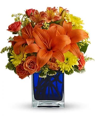 Summer Nights by Teleflora - Flower power rises several degrees in this brilliant array of hot summer flowers in a cool blue contemporary glass cube vase. Send this gift of indoor sunshine to someone close to you. The radiant bouquet includes orange Asiatic lilies, orange alstroemeria, yellow cushion spray chrysanthemums, solidago and orange spray roses accented with assorted greenery. Delivered in a blue contemporary glass cube vase.
