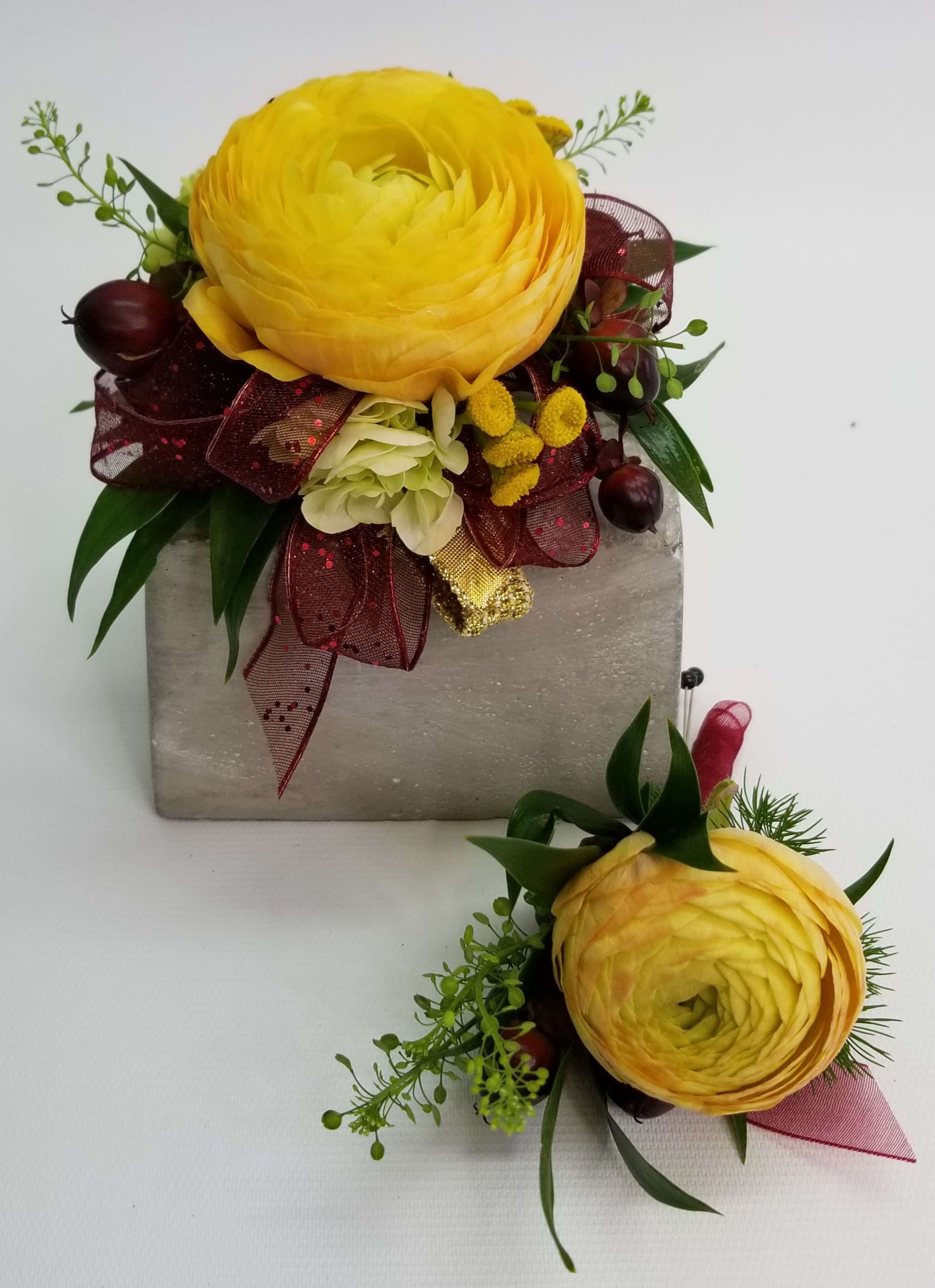 Yellow Corsage and Bout Set Yellow Corsage and Bout Set - Yellow Ranunculus, green hydrangea, yellow accents and greens. Deep burgundy ribbon, standard elastic wristlet. Corsage and boutonniere set.