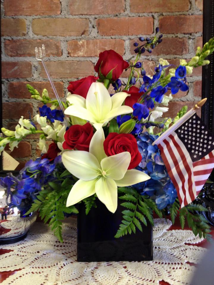 Thank a Veteran Thank a Veteran - Beautiful white lillies, eye catching blue delphinium along with a blue hydrangea, red roses and white snaps proudly fill this blue vase along with The American Flag