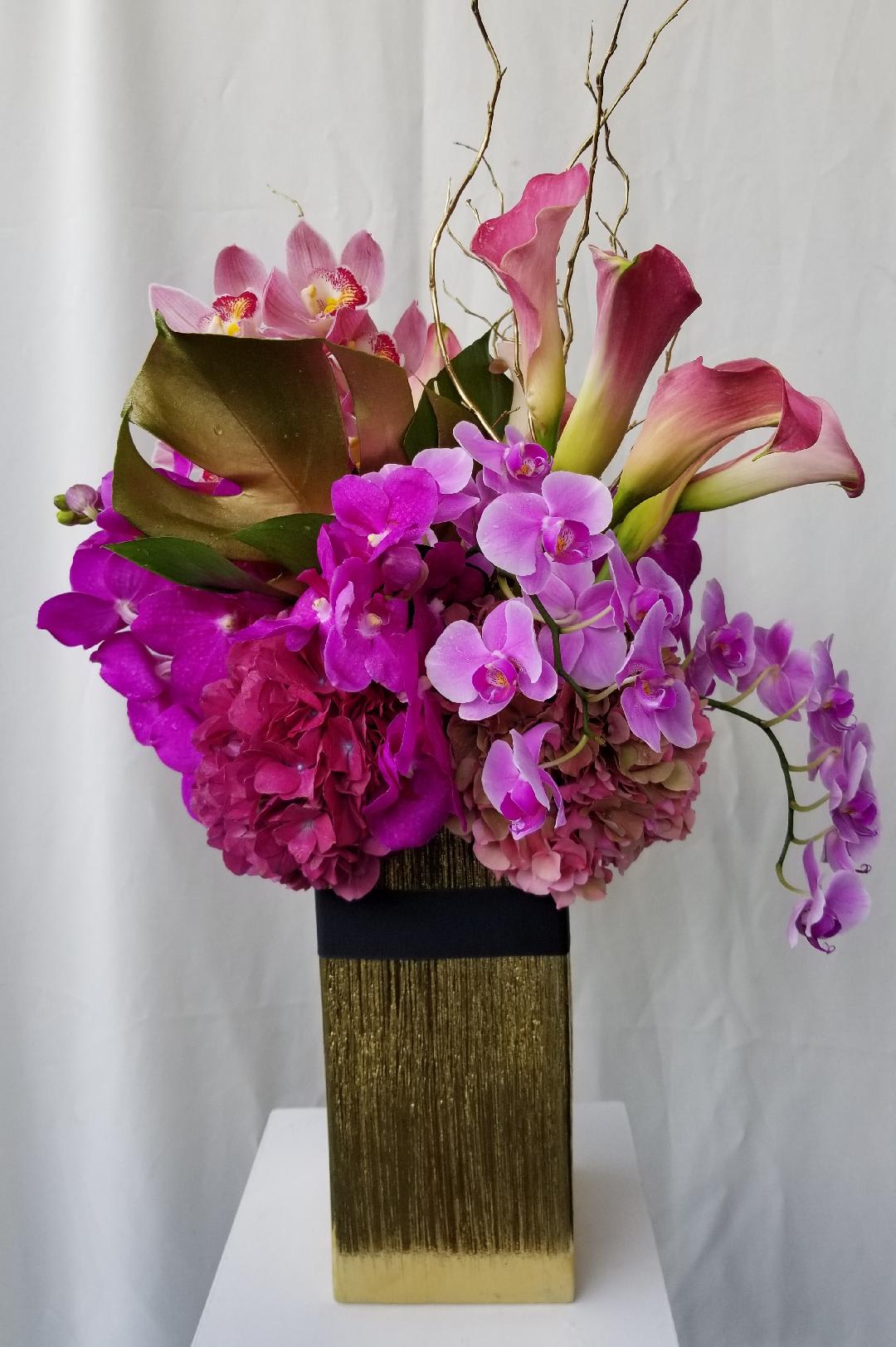 Vibrant Adele Vibrant Adele - Brighten someone's day, week, and month with our stunning arrangement boasting vibrant pink and lavender tones. Standing elegantly in a decorative container, this arrangement features exquisite Calla lilies, enchanting Cymbidium Orchids, fresh Hydrangeas, and a delicate touch of curly willow. At Dave's Flowers, we specialize in creating enchanting floral masterpieces that evoke joy and delight in every moment. The captivating blend of pink and lavender hues creates a visually striking display that radiates warmth and sophistication, making it an ideal gift for all occasions. The graceful Calla lilies exude timeless elegance, while the enchanting Cymbidium Orchids add a touch of opulence and refinement. Enhanced by the freshness of the Hydrangeas and the whimsical allure of curly willow, this arrangement embodies the perfect balance of grace and natural beauty. Our skilled florists meticulously craft each element, ensuring that every detail is thoughtfully curated to convey your heartfelt emotions and sentiments. With our seamless online ordering and prompt delivery service, sending a thoughtful and vibrant floral gift has never been easier. Discover the magic of our vibrant pink and lavender tones arrangement at Dave's Flowers and let us be your trusted partner in creating unforgettable moments filled with the beauty and freshness of nature's finest creations.