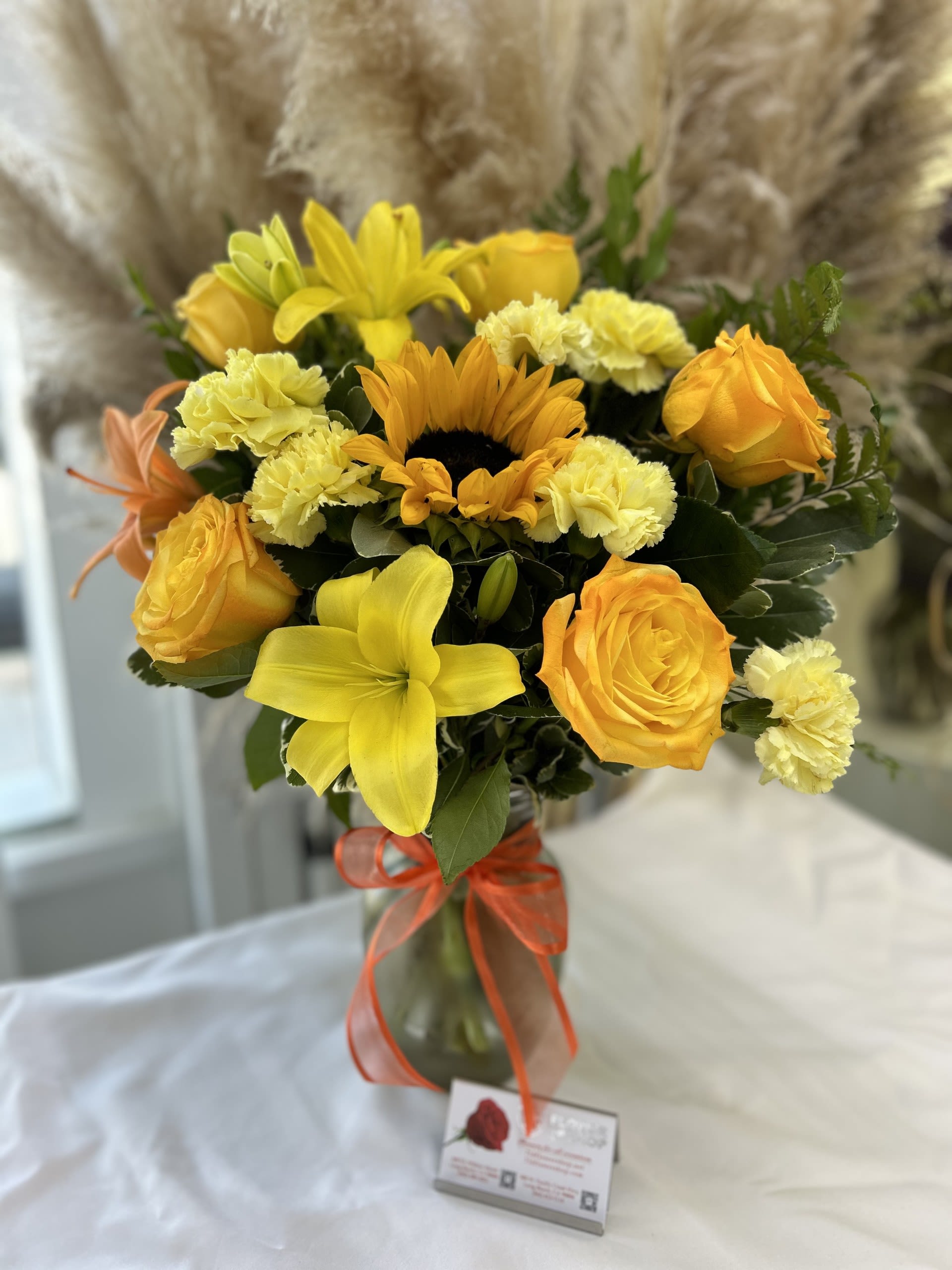 Golden Glow Golden Glow - This vibrant arrangement with its sunny yellows and oranges, highlighted by a beautiful sunflower, exudes warmth and happiness. Substitutions: If some flowers and/or the vase are not available there will be minor substitutions.