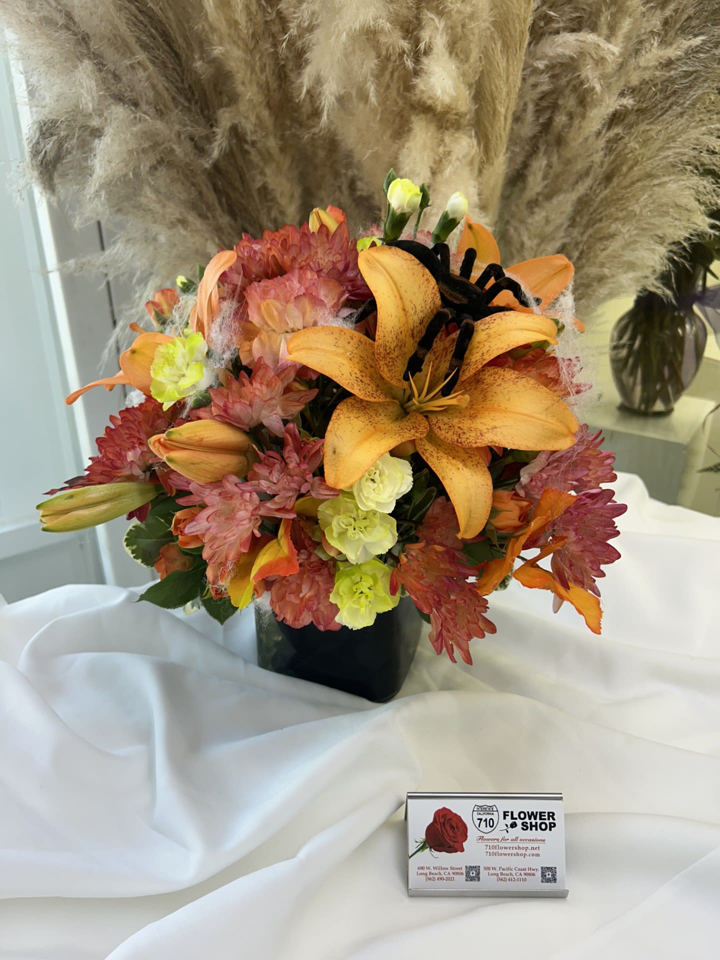 Spooky Harvest Bloom - The combination of vibrant autumn colors and the playful spider detail brings together the spirit of the season with a touch of elegance If some flowers and/or the vase are not available there will be minor substitutions.