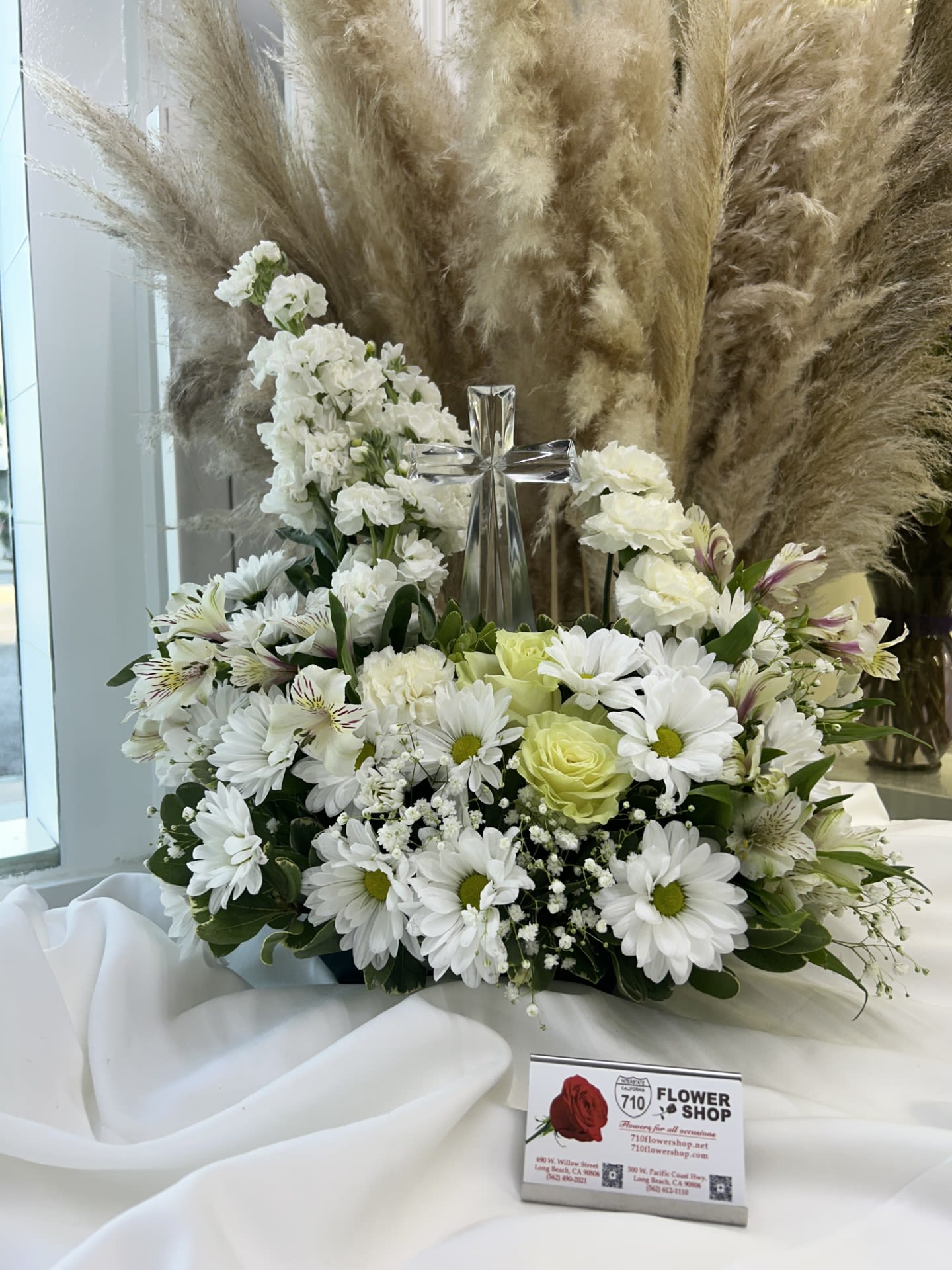 Heaven’s Grace - The soft white daisies, roses, and the prominent cross create a sense of serenity and spiritual beauty. It feels like a tribute to purity and peace. Substitutions: If some flowers and/or the vase are not available there will be minor substitutions. 