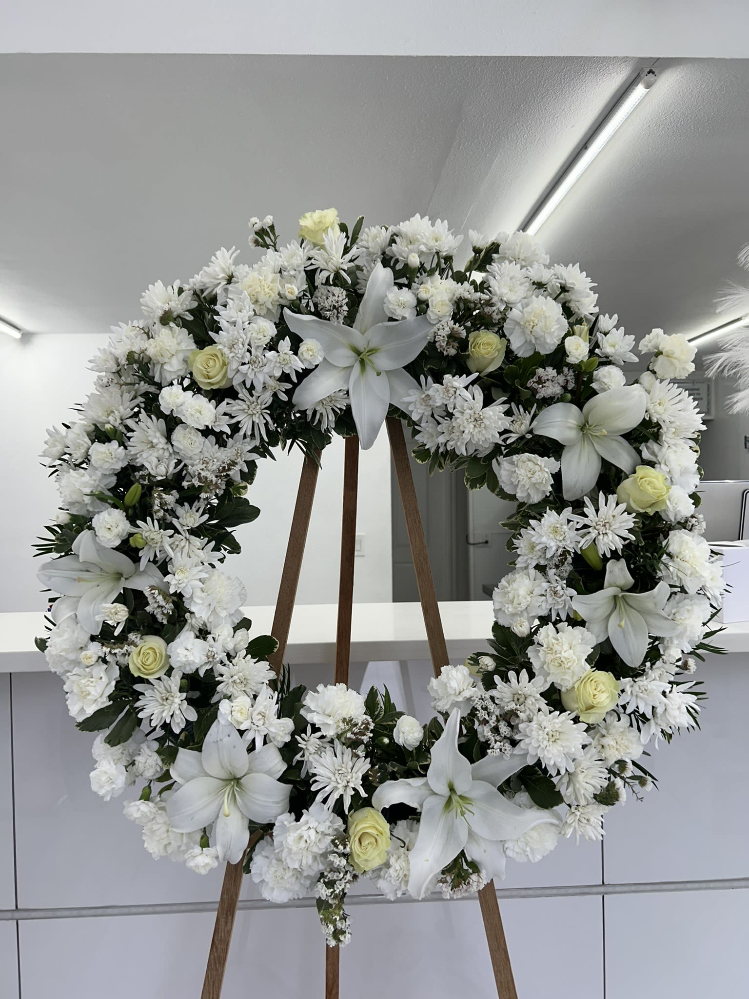 Peaceful Grace  - This elegant white wreath, with its delicate lilies and roses, evokes a sense of purity, peace, and grace.  If some flowers and/or the vase are not available there will be minor substitutions