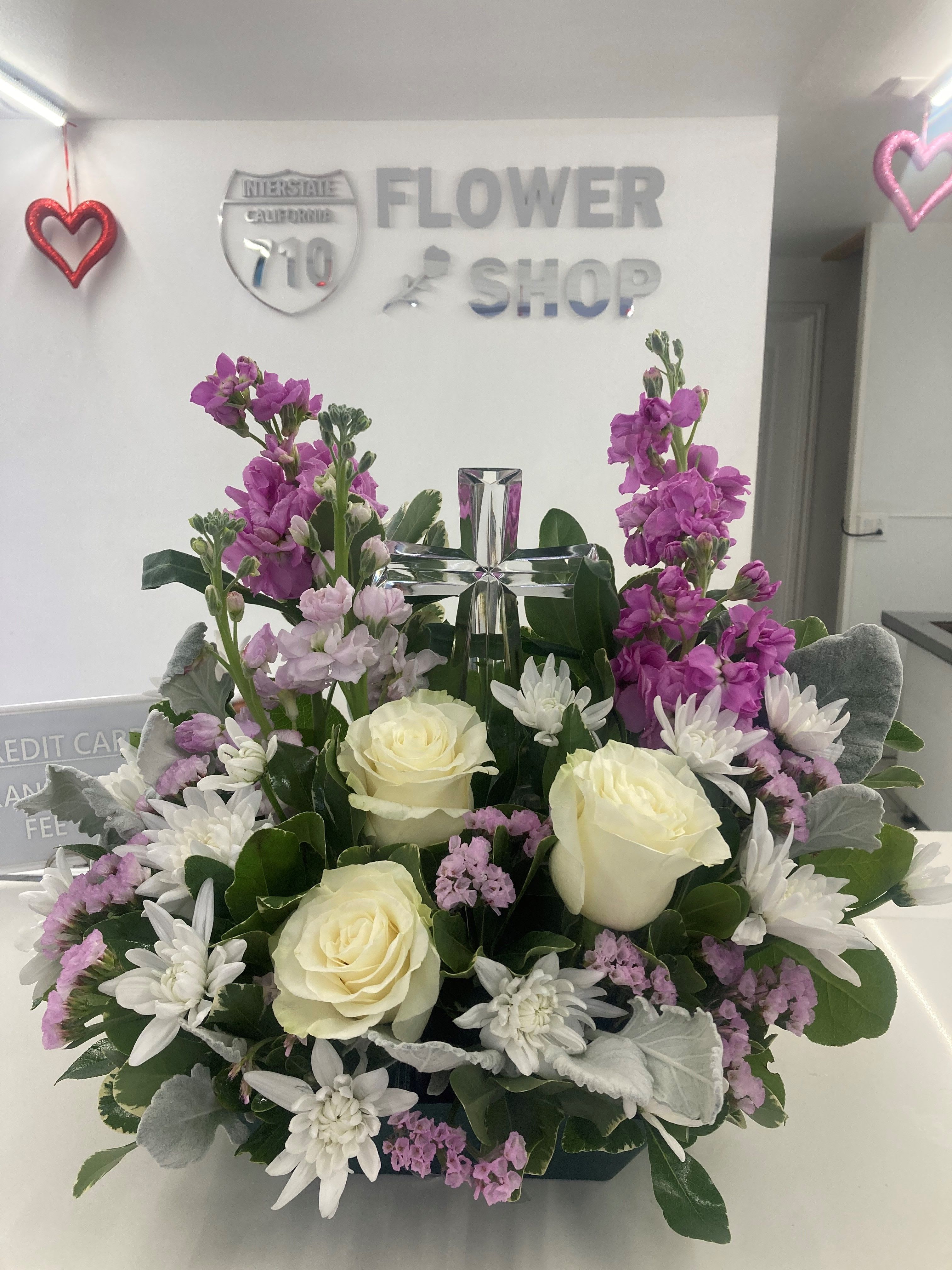 Graceful Serenity  - Soft white roses, delicate purple flowers and a crystal cross centered. (If you'd like this arrangement in a certain color please leave a note in the instructions) Substitutions: If some flowers and/or the vase are not available there will be minor substitutions.  