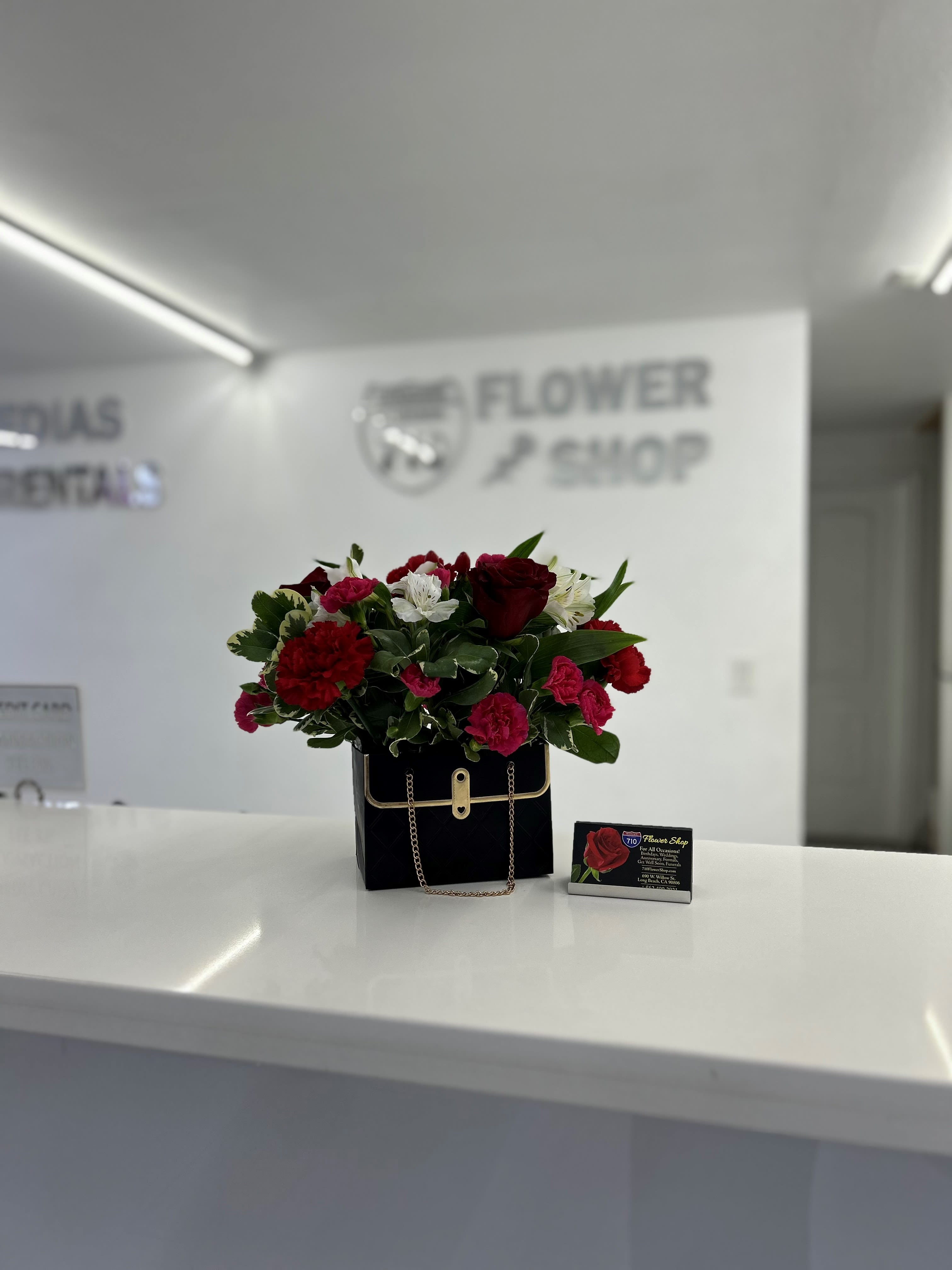 Black Purse Arrangement  - A cute black purse arrangement with beautiful flowers! Comes included with valentines day sign! Heart Box comes in Pink, Black, and White with a mixture of flowers. If you'd like a specific color please leave note in instructions! (Chose your choice of color. If we do not have the same sign, chosen box color available or the same flower as photo we will add substitute for next available) Substitutions: If some flowers and/or the vase are not available there will be minor substitutions.