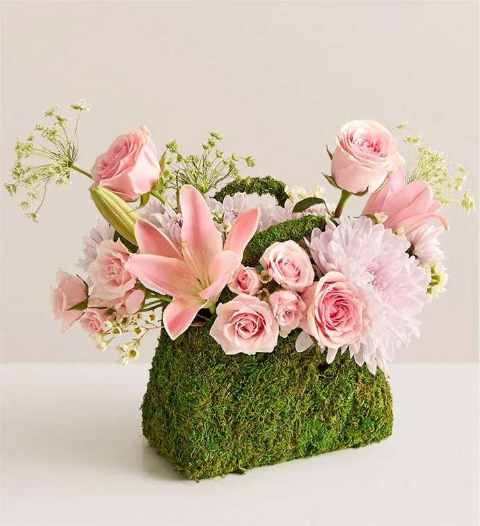 Palermo Blush Pink and Lavander  - Palermo Blush This just might be the most fashionable, and Insta-worthy, bouquet ever. An eye-catching array of pink roses and other blooms burst forth beautifully from a planter shaped like a handbag and clad in preserved moss. After the blooms are gone, the planter will retain its elegance, making this a truly timeless gift.  One-sided arrangement of pink roses, spray roses, and cushion poms; a pink hybrid lily and disbud mum; and white Queen Anne’s lace and waxflower Artistically designed in a handbag-shape container covered in preserved moss Measures approximately 12”H x 11”L Our florists hand-design each arrangement, so colors and varieties may vary due to local availability To ensure lasting beauty, lilies may arrive in bud form and will fully bloom over the next few days