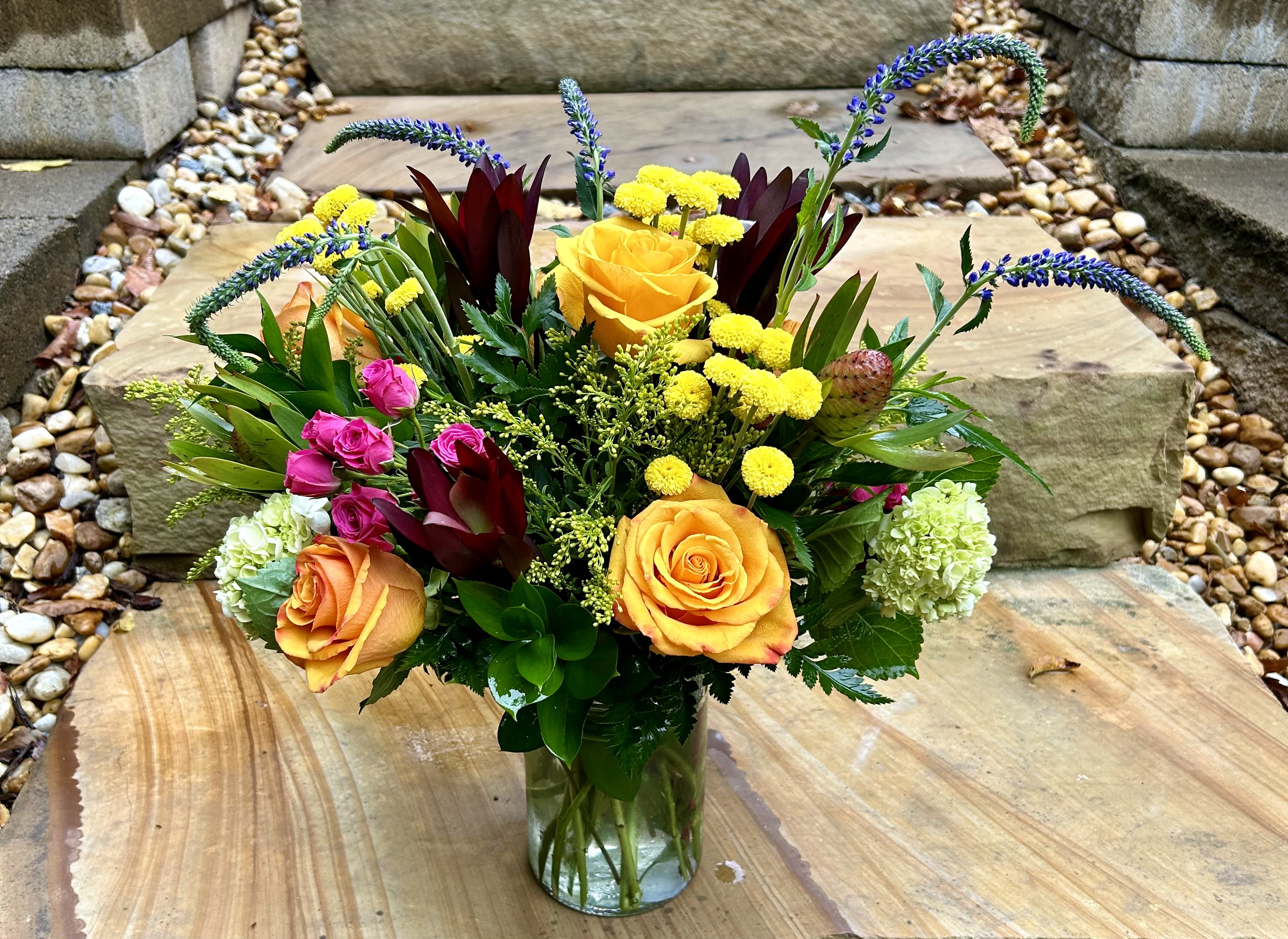 Alluring Sunshine - A fresh and airy arrangement of yellows, orange, pinks, purples, reds and greens designed in a glass vase. 