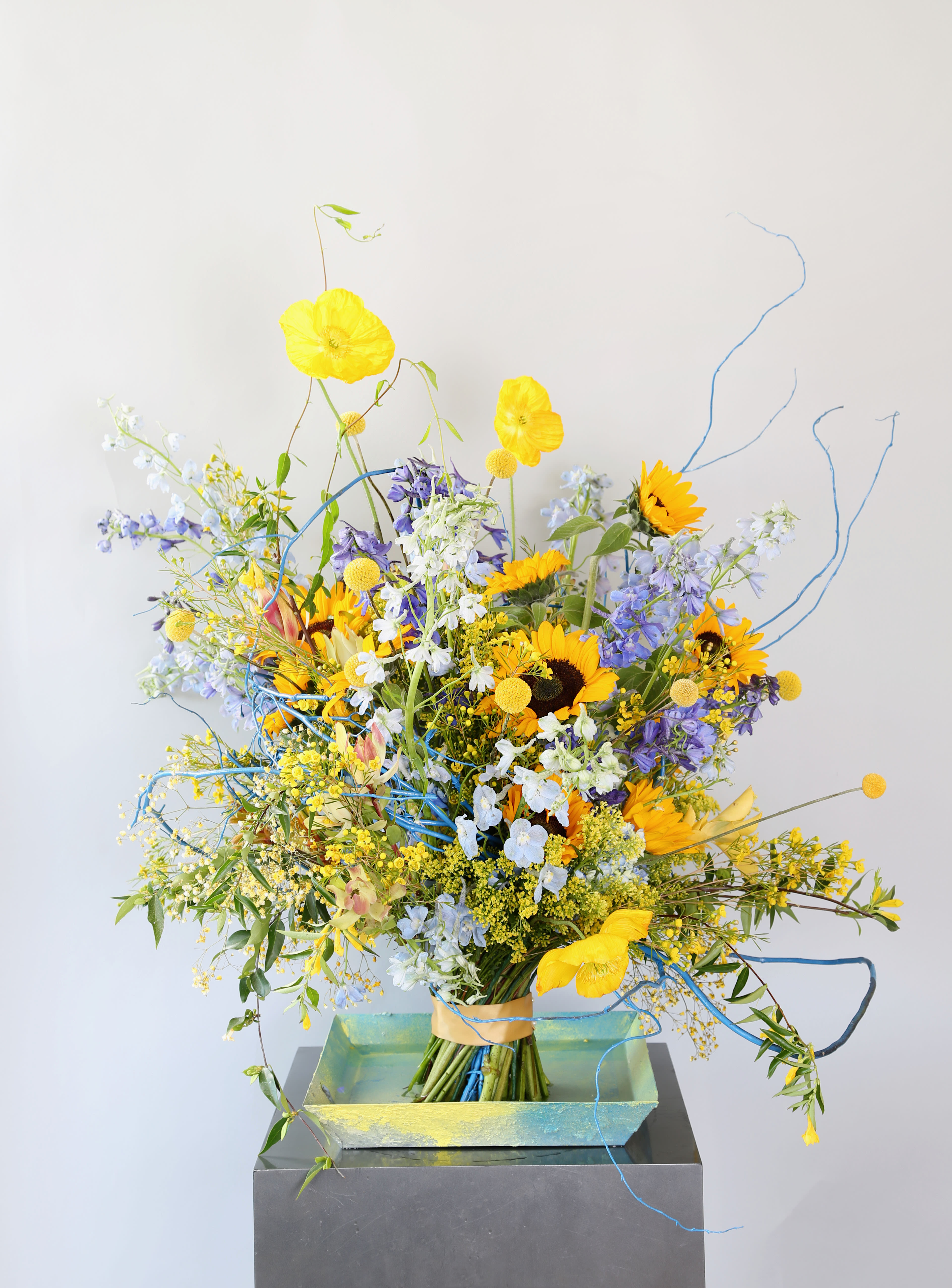 Blessing - We will donate $100 dollars of each order for this arrangement to www. UUARC.org to help the people who suffer in Ukraine. This sculpture handtie Bouquet creation is inspired by Ukraine war bu using Sun flower, Delphinium,Hydrangea with seasonal bloom in yellow and blue colorway. This huge hand tie arrangement come with 7&quot; tall vase