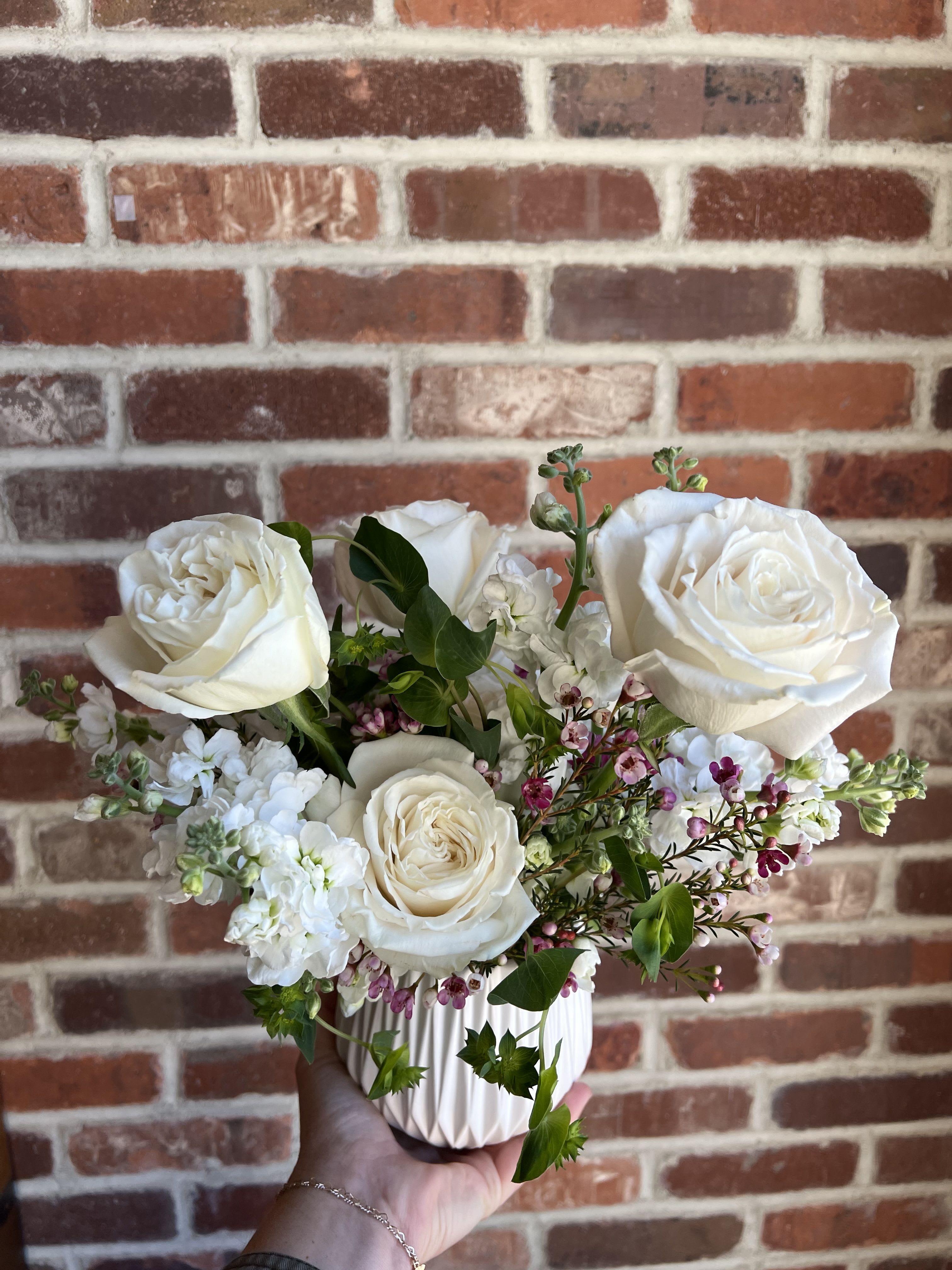 Pure and Simple White Floral Arrangement Pure and Simple White Floral Arrangement - Understated and serene, our "Pure & Simple" arrangement features a graceful selection of fresh white blooms artfully arranged in a minimalist ceramic white vase. This timeless design highlights the natural beauty of each flower — from delicate petals to soft textures — creating a look that’s both clean and calming. Perfect for modern interiors, sympathy gestures, or any occasion that calls for quiet elegance, this arrangement brings a sense of peace and refinement to any space. Each piece is made to order with fresh, seasonal white flowers. Available for local delivery, events and pick up.
