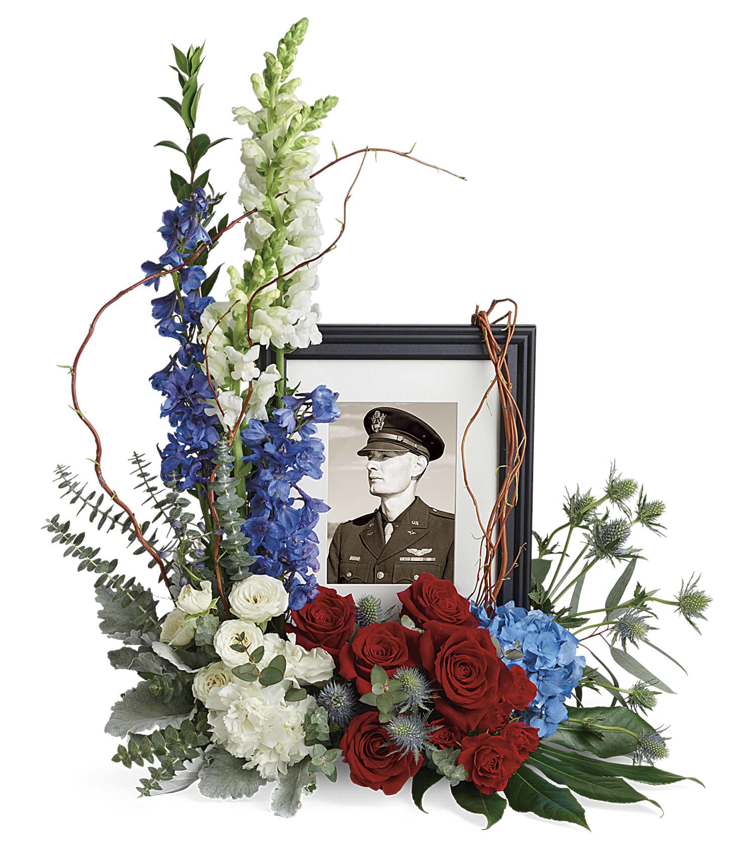Always With Us Photo Tribute Bouquet - Honor the memory of an always-beloved with this beautiful display bouquet. Designed to surround a favorite photo, its patriotic mix of blue hydrangea with red and white roses is a respectful tribute.  This bouquet features blue hydrangea, red roses, red spray roses, white spray roses, white carnations, blue delphinium, white snapdragons, blue eryngium, dusty miller, curly willow, spiral eucalyptus, parvifolia eucalyptus, aralia leaf and lemon leaf. Arrangement does not include picture frame.    T282-1A    