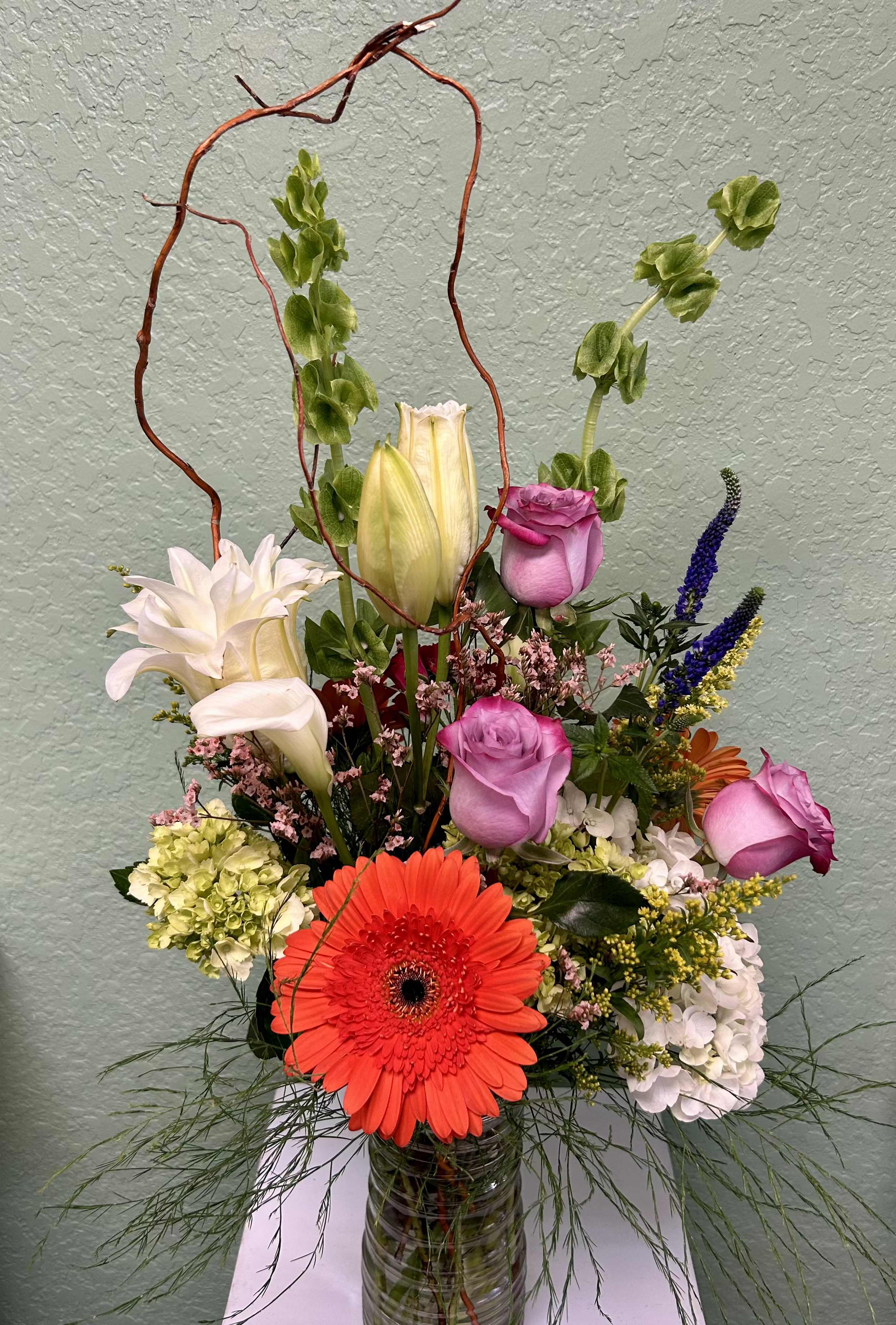 CFM131 CFM131 - A tall vibrant spring mix bouquet of flowers such as lilies, roses, bells of ireland, hydrangea and gerber daises.