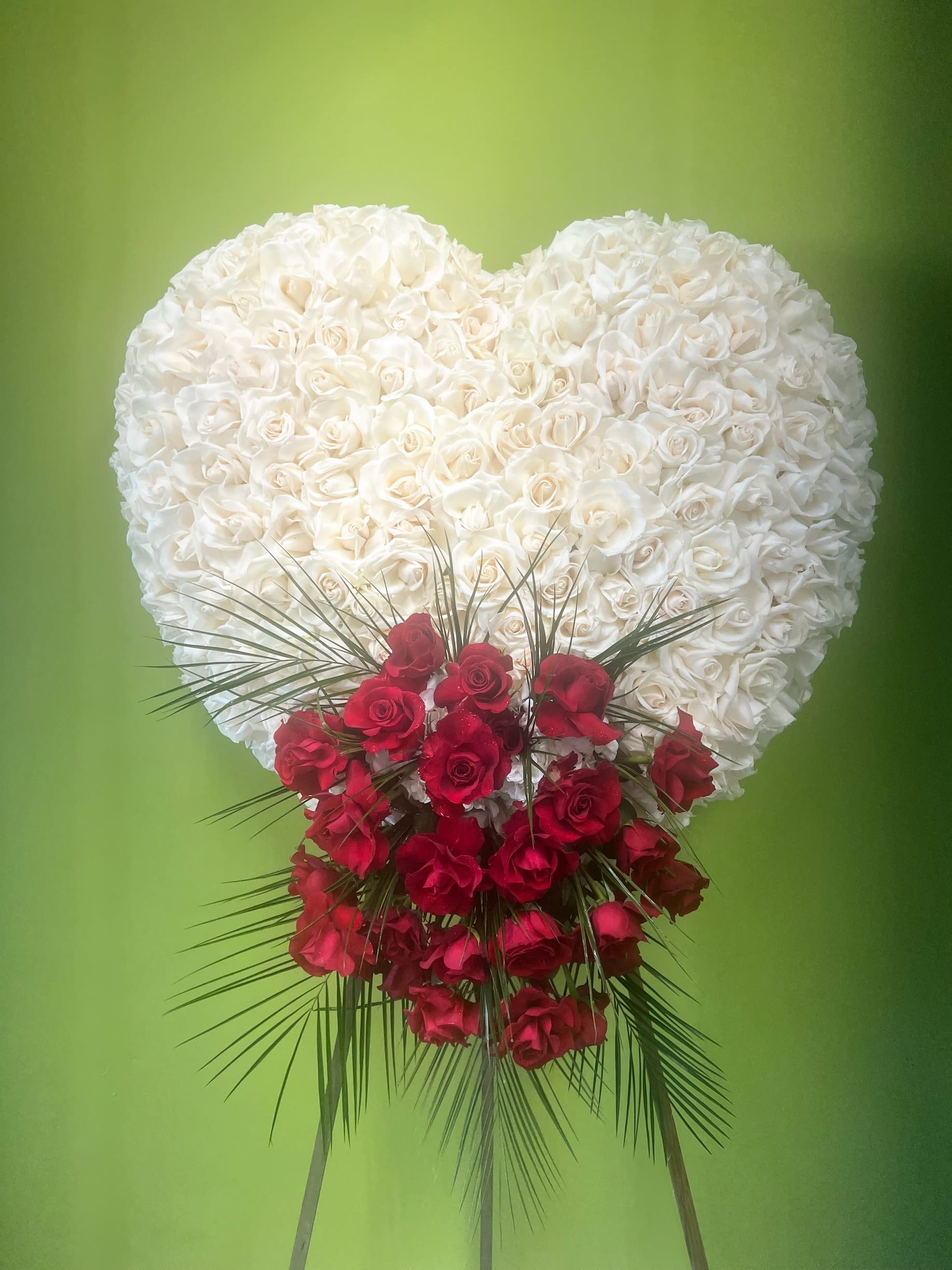 Pure Love Heart Tribute Pure Love Heart Tribute - A breathtaking white rose heart adorned with a cascading spray of red roses and lush greenery. This standing funeral heart is a timeless tribute of love, respect, and everlasting memories.