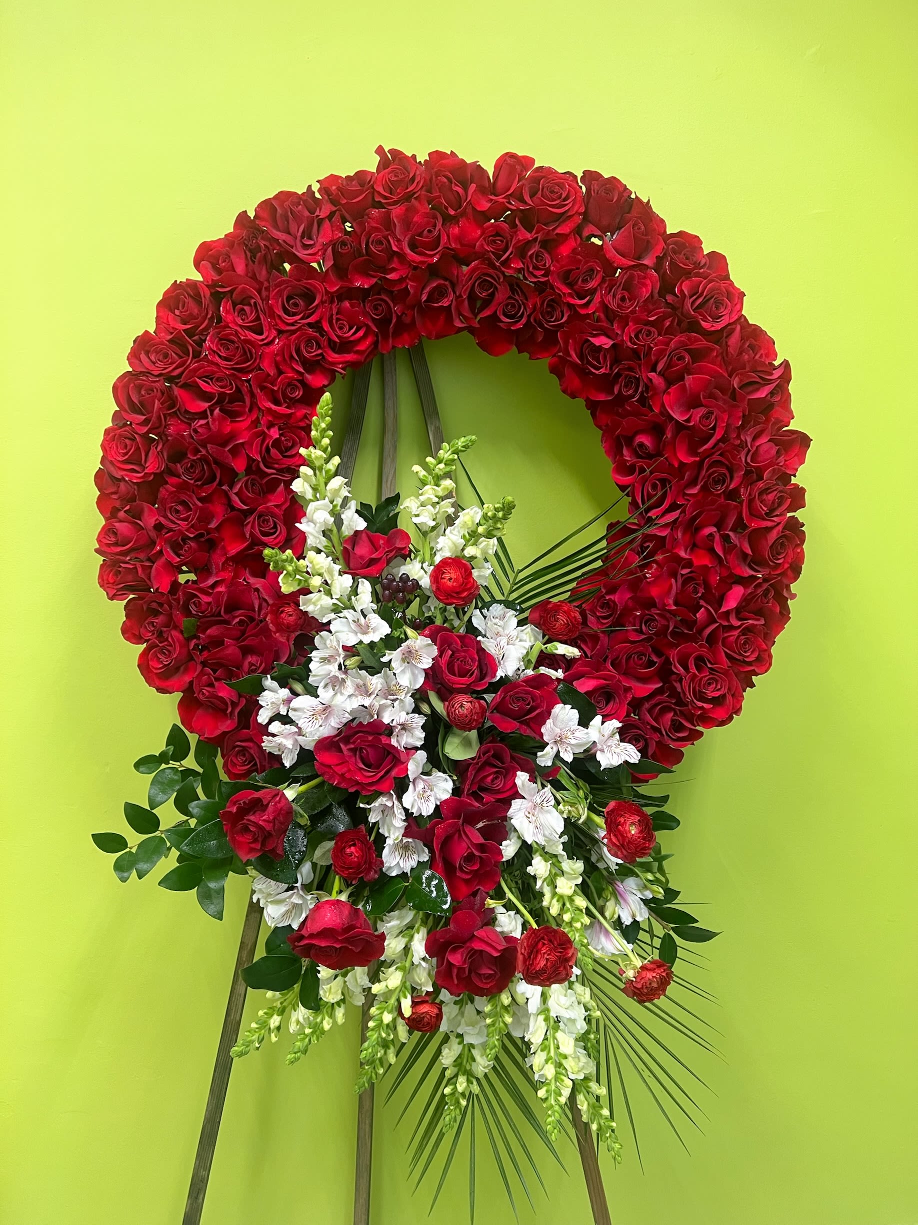 Remembrance Glory Wreath Remembrance Glory Wreath - A grand red rose wreath with a cascading mix of white flowers, greenery, and soft floral fillers, creating a classic and elegant funeral tribute.