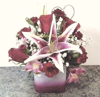 Be Mine - A beautiful 4x4 cube vase filled with stargazier lilies, roses, wax flower and other assorted flowers with a wired heart pick.  Please note*Cube vase may vary in color 