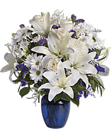Beautiful in Blue Arrangement Beautiful in Blue Arrangement - crème roses, graceful white oriental lilies, white alstroemeria, a white disbud mum, purple statice and lavender limonium are accented by seeded eucalyptus and salal in a stunning cobalt blue glass vase.