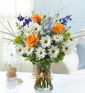 By The Seashore Flower Arrangement - This is an awesome design for those who love and live by the beach. It's beautiful with tones of blue delphinium, coral roses, white daisies and bear grass.