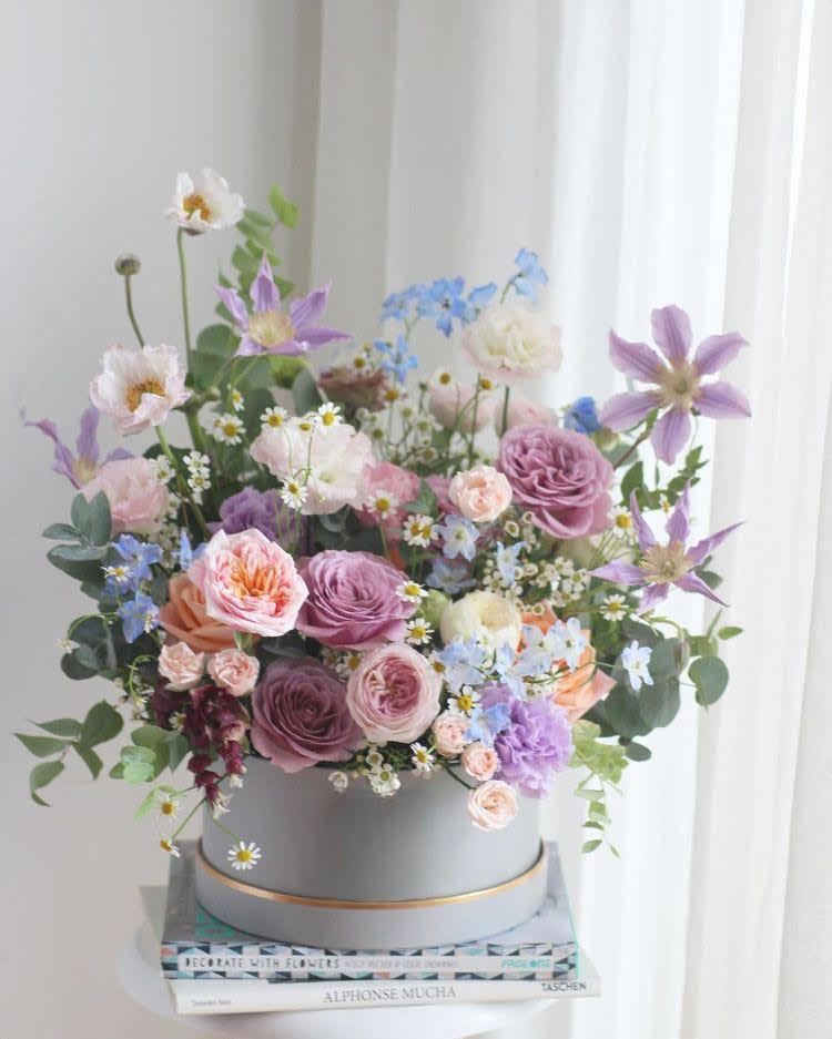 Whispers of Serenity Whispers of Serenity - Bring serenity into your life with "Whispers of Serenity", a captivating flower arrangement that exudes calmness and refinement. This exquisite bouquet, nestled in a stunning hat box, showcases a delicate balance of pastel hues and lush blooms. Soft pink, purple, and white flowers entwine with greenery, creating a soothing visual harmony that will tranquilize your senses. Perfect for any occasion, "Whispers of Serenity" is a thoughtful gift or a beautiful addition to your home, promising to bring peace and joy to all who behold it. Let its gentle beauty calm your mind and soothe your soul.