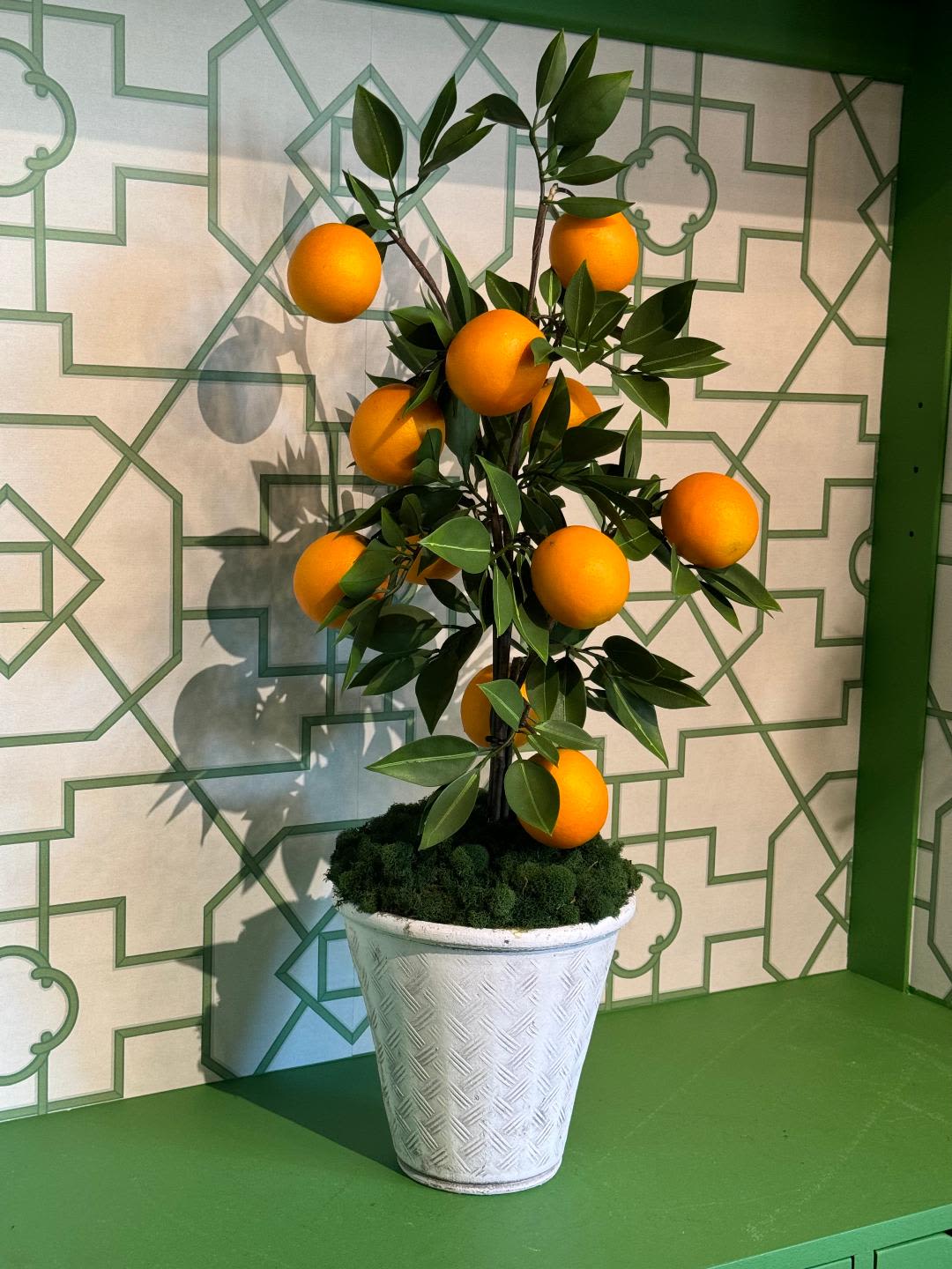 Faux Orange Tree - Bring a touch of Mediterranean charm into your space with this realistic, high-quality faux orange tree. Carefully crafted to replicate the vibrant leaves and lifelike oranges, this tree is accented with moss for an added natural touch. Set in a soft grey ceramic pot, it offers timeless style and a refreshing pop of color, perfect for brightening any room. Ideal for low-maintenance decor, this faux tree requires no watering or sunlight, making it a perfect addition to your home or office.  Please note: Due to the nature of faux plants, slight variations in color and appearance may occur, ensuring each piece is unique.