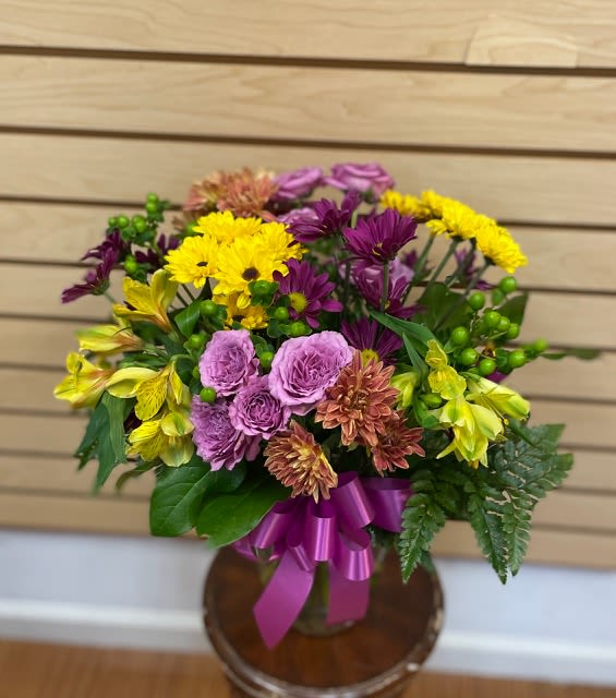 Sassy Waves - Mixed cut arrangement with golden cushion mums, yellow alstroemeria, lavender spray roses, purple daisies, and green berries in vase