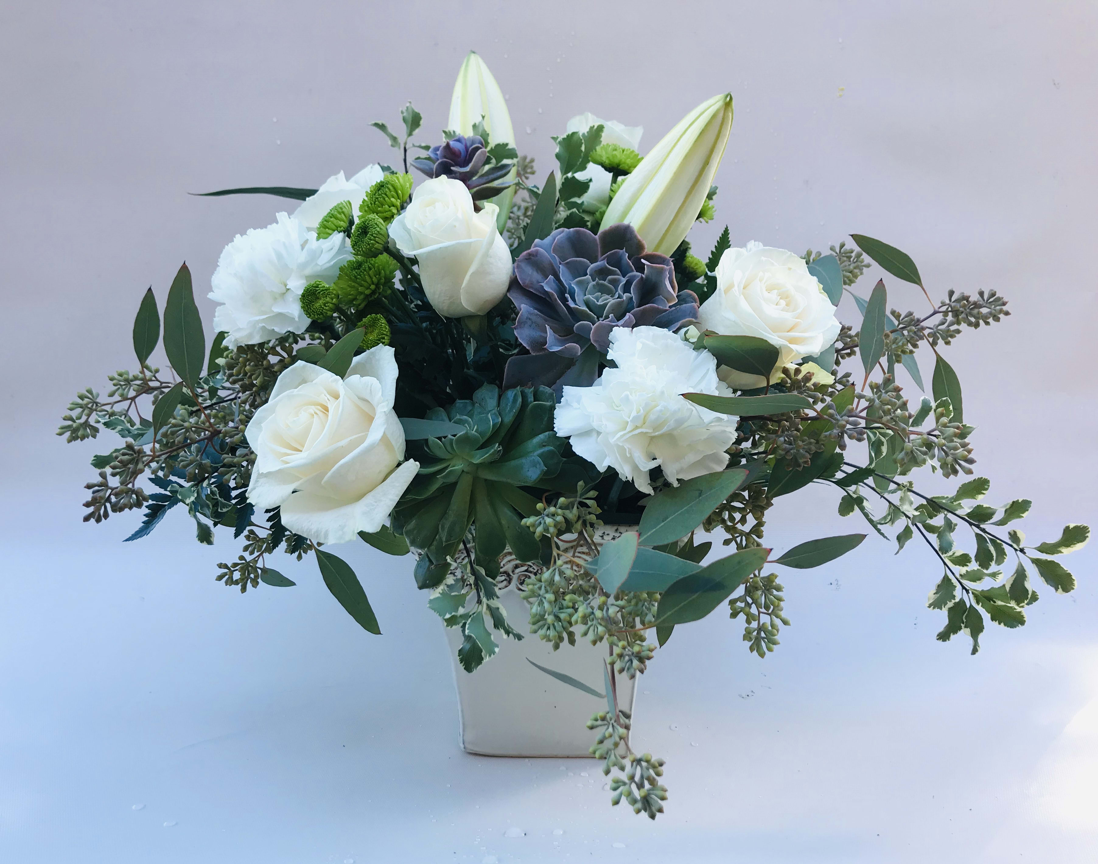 Blissful Desert Garden - This elegant arrangement sits in a ceramic container and includes live succulents, white and cream flower: roses, carnations, oriental lilies and a dash of green buttons. Seeded eucalyptus and a variegated green to compliment the succulents give a serene feel.  NOTE: The succulents will not always be the exact ones as seen in the photo. They come in different varieties of colors and plants, but the overall look will be the same. 