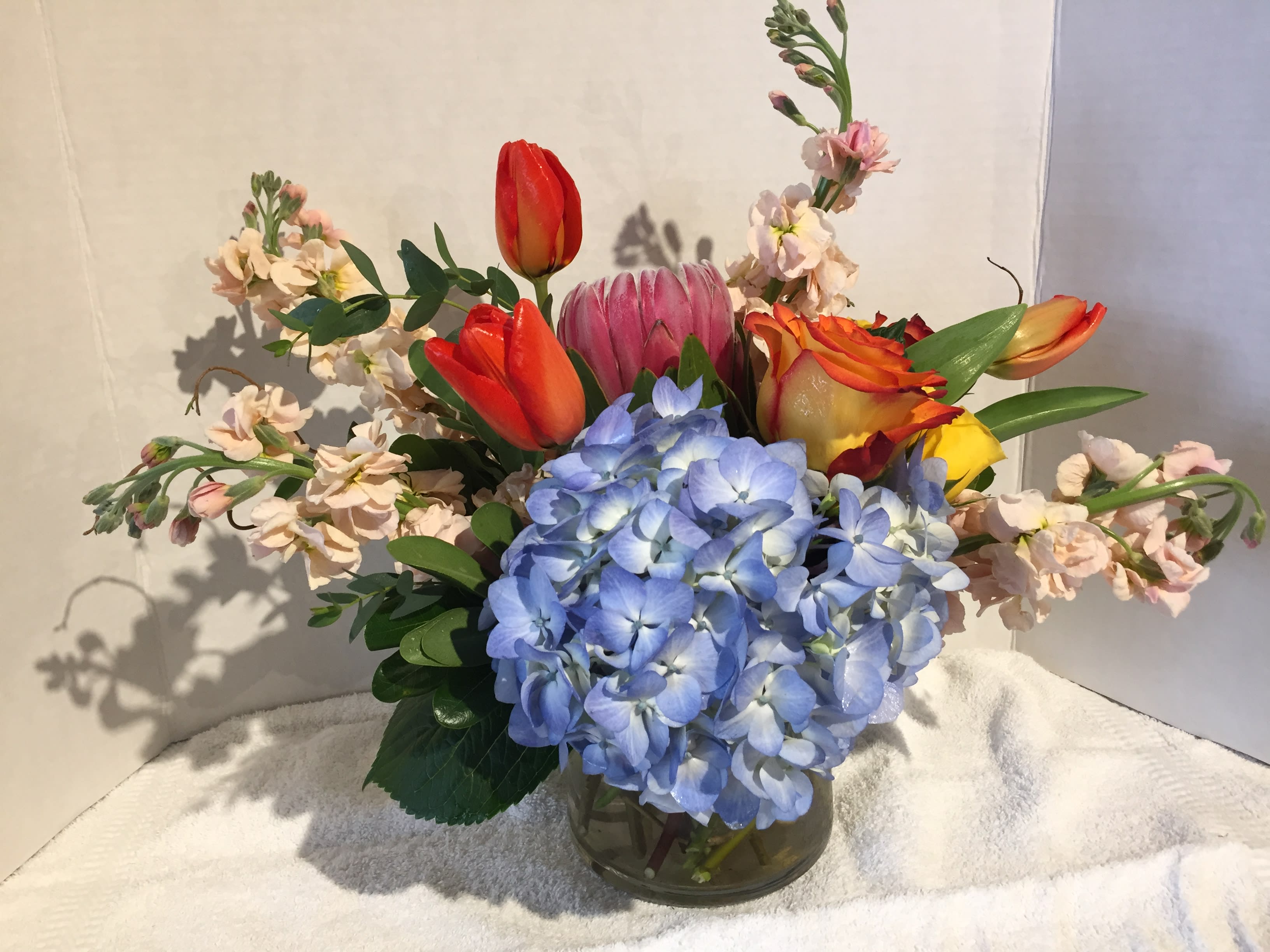 Blue Skies! - This cheerful arrangement is perfect for the unique flower lover. A mix of spring flowers with mink protea and hydrangea.  Pictured is Roses, Hydrangea, Mink Protea, and Stock. Your arrangement will be designed in the style shown, but flowers and containers may be different from that pictured.