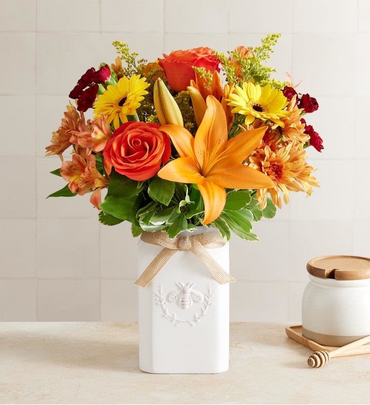 Honey Bee Buzz™ for Fall Honey Bee Buzz™ for Fall - Get them buzzing for fall! Our unique, stylized bouquet is gathered with a mix of blooms in warm yellow, orange, bronze and burgundy. Designed in our Sweet As Can Bee artisanal vase, featuring an adorable honey bee and raffia bow, it’s a gift that adds seasonal beauty to any décor. All-around arrangement with orange roses, Asiatic lilies, Peruvian lilies (alstroemeria), yellow mini Gerbera daisies, bronze cushion poms, burgundy mini carnations; accented with assorted greenery Artistically designed in our Sweet As Can Bee vase, crafted in white ceramic, accented with an embossed honey bee crest and finished with a raffia bow; measures 4.13"L x 4.13"W x 7"H Our florists hand-design each arrangement, so colors and varieties may vary due to local availability To ensure lasting beauty, Peruvian lilies may arrive in bud form and will fully bloom over the next few days
