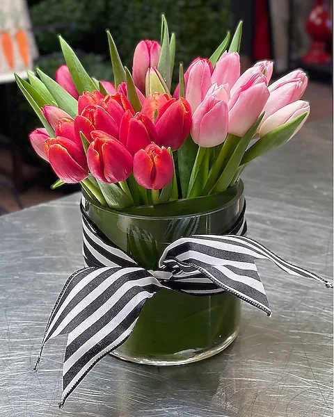 Tulip Joy - Five bunches of tulips arranged with the simplicity of a clear glass cylinder, an accent ribbon tie, and a ti-leaf wrap. NOTE: Colors may vary from photo and are chosen by designer based on best quality and colors available. If exact colors are needed, contact the store to place order.  All prices in USD ($)