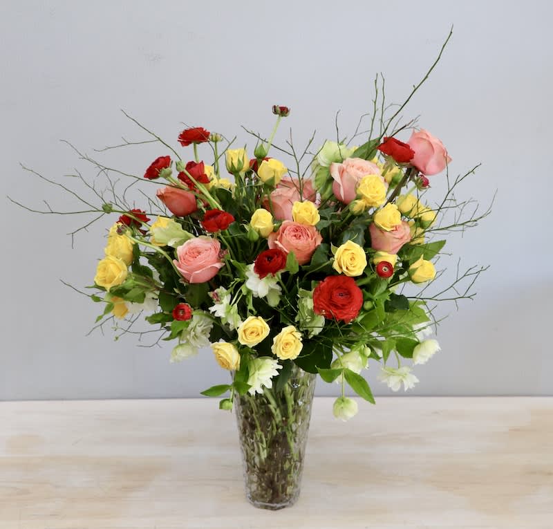 Springtime Sunrise - WeHo Springtime Sunrise - WeHo - This arrangement is filled with vibrant red ranunculus, yellow spray roses, peach roses, and graceful hellebore. All made in a lovely tall vase.