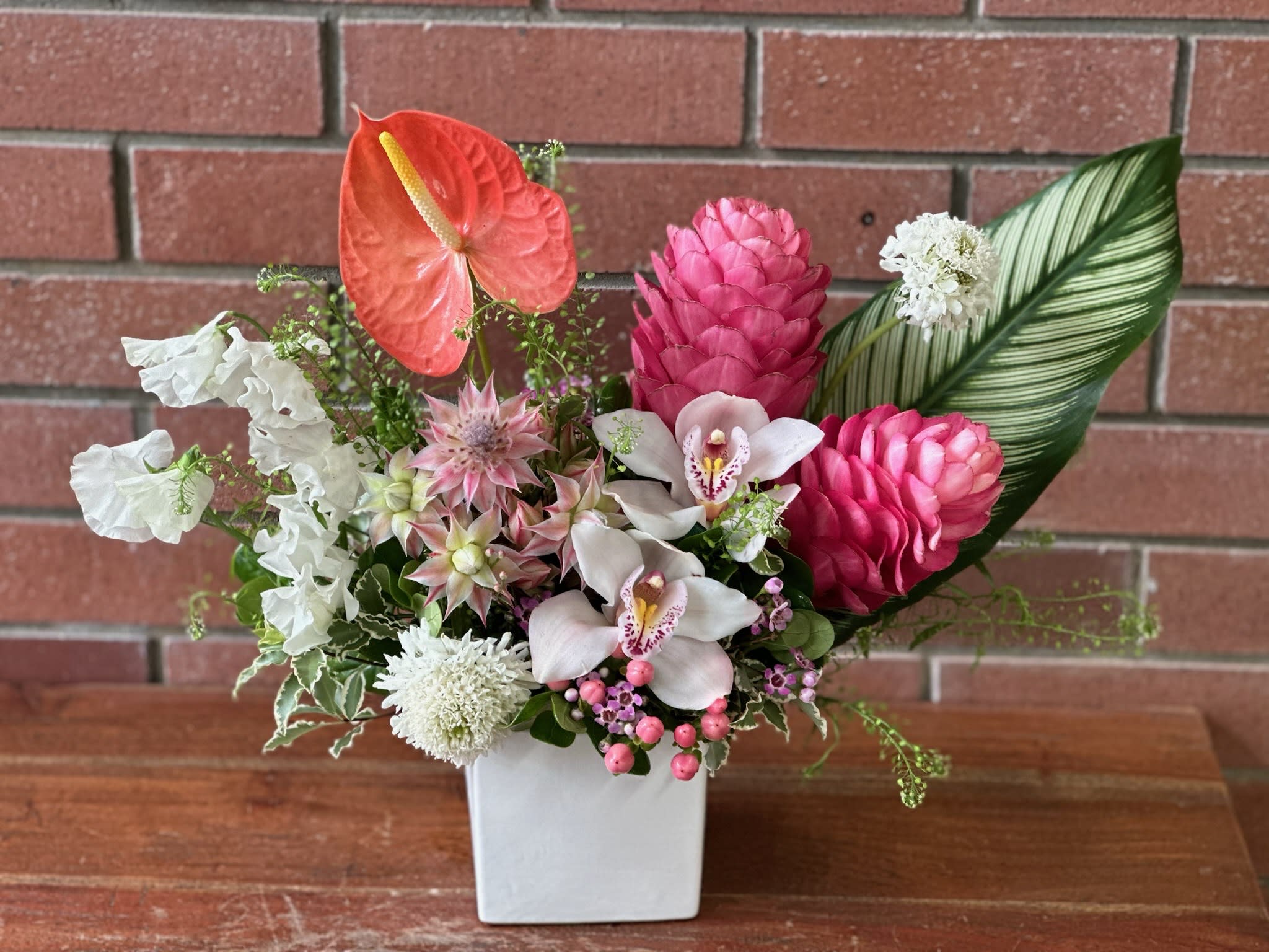 Summer Tropical Arrangement of the Week Summer Tropical Arrangement of the Week - Sweet Pea, Pink Ginger, Orchids, Anthurium, Blush/White, Tropical Arrangement. In a Ceramic Glass.