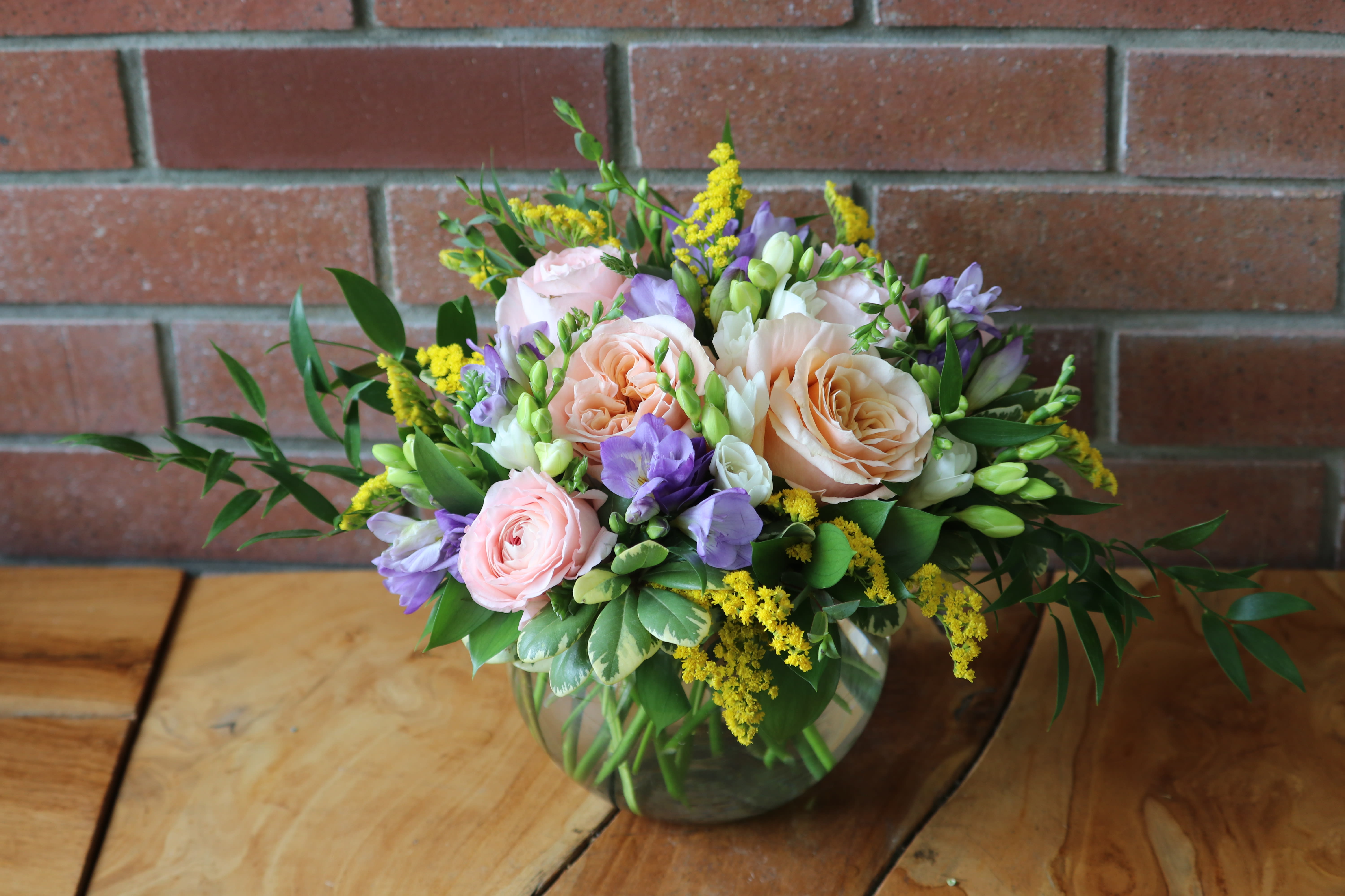 Summery Blooms Summery Blooms - Gorgeous peach roses, ranunculus, fresh fragrant freesia, yellow solidago and italian ruscus in a glass bubble bowl