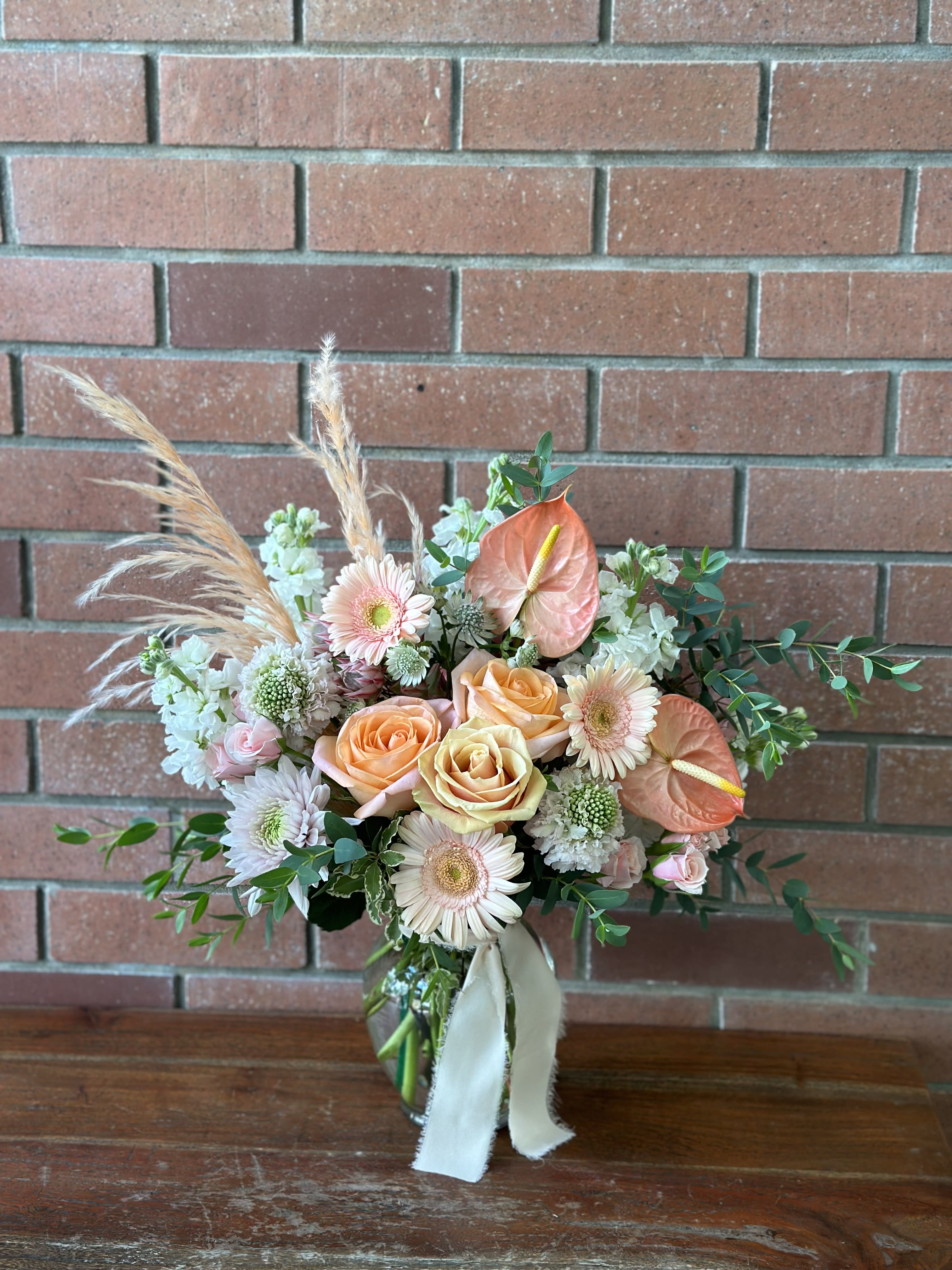 Peach Perfect  - Our finest peachy selections - premium peach anthurium, roses, spray roses, scabiosa, miniature peach gerbers accented with lush white stock flowers, pampas’s grass, wispy eucalyptus and more in a clear vase. 