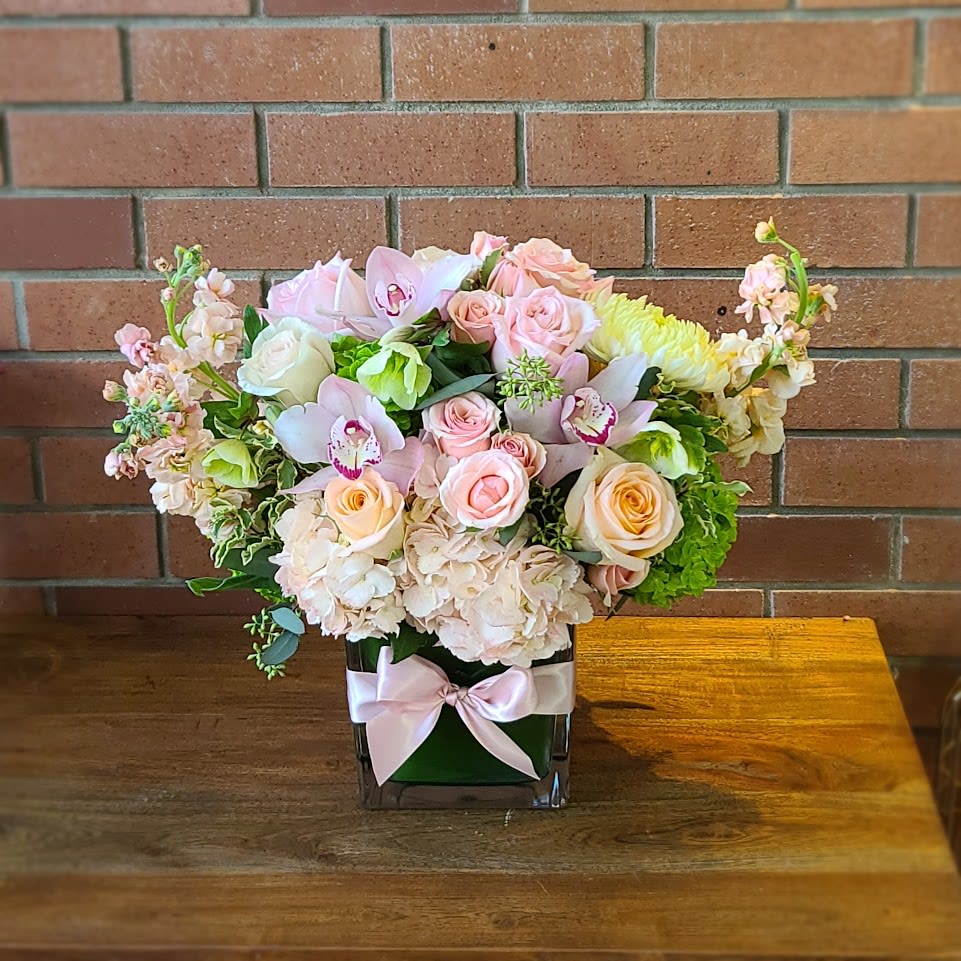 Flowers For Mom Bouquet - Send a lovely arrangement of hydrangeas, roses, orchids, helleborus, peach stock, pink orchids and lovely ball chrysanthemums designed in a clear cube wrapped with a green leaf and a pretty pink bow 