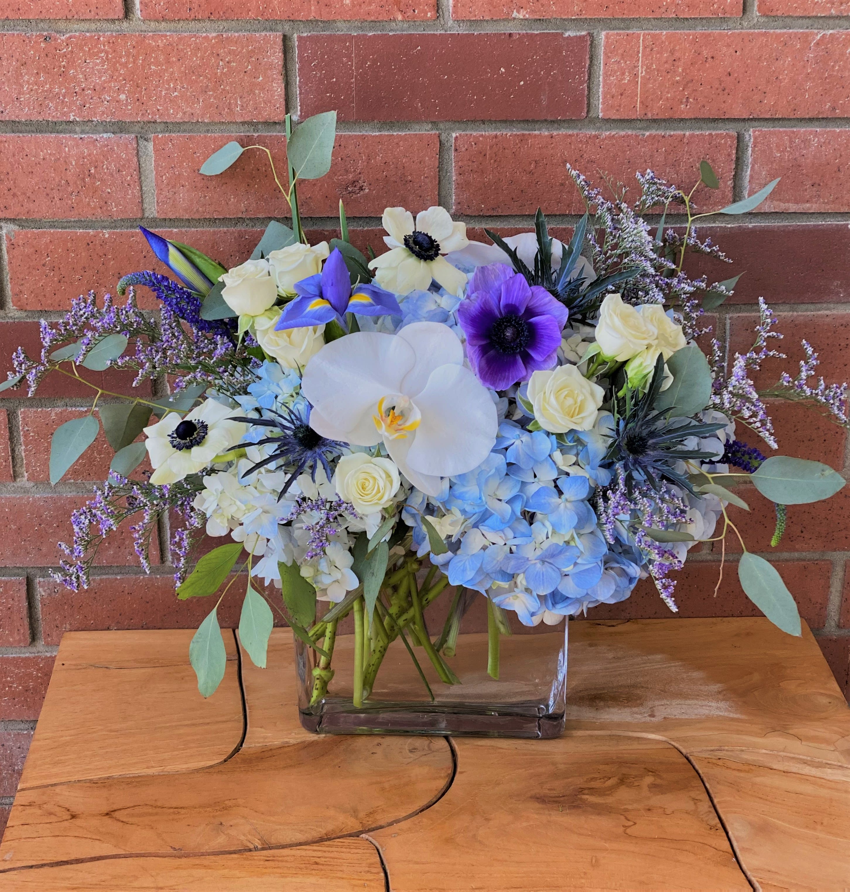 Clear Skies Bouquet - Blue hydrangea, orchids, anemones, spray roses, iris, thistle, eucalyptus and premium fillers arranged in a modern 6 inch rectangular glass vase. Pictured size &quot;Standart&quot;